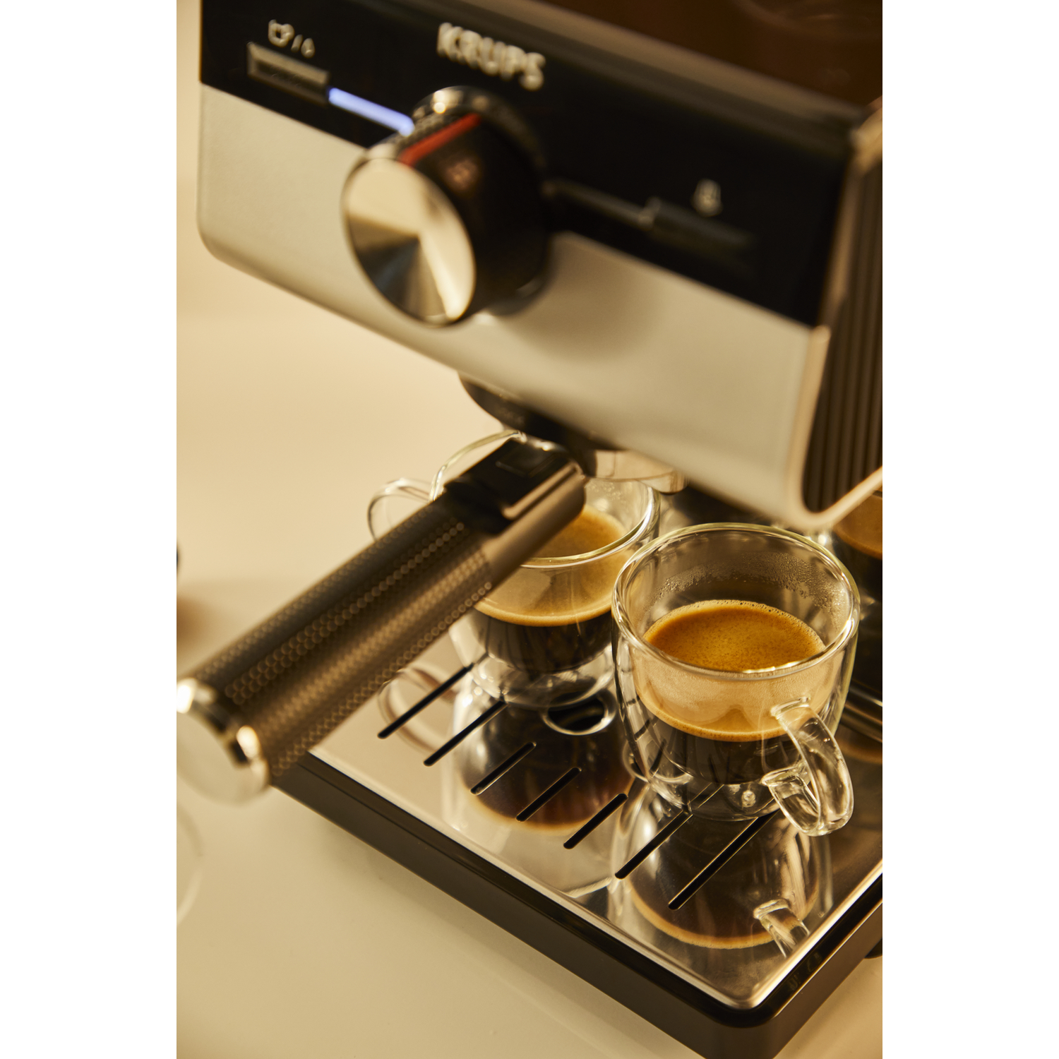 Koffiemachine die koffie uitschenkt in twee heldere glazen kopjes, op een wit oppervlak.