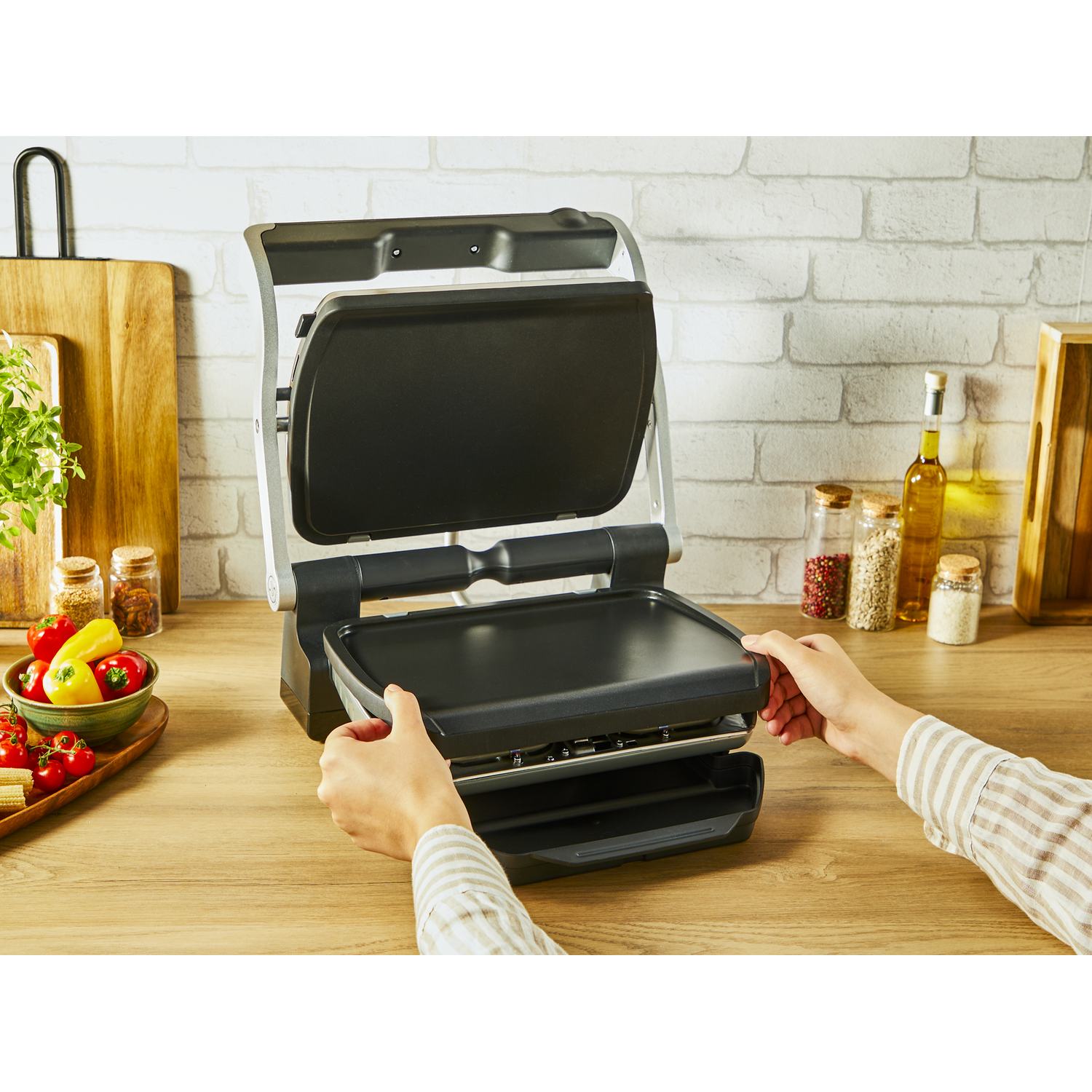 Hands assembling a black grill, with food items on the table. Wood cutting boards and spices are present.