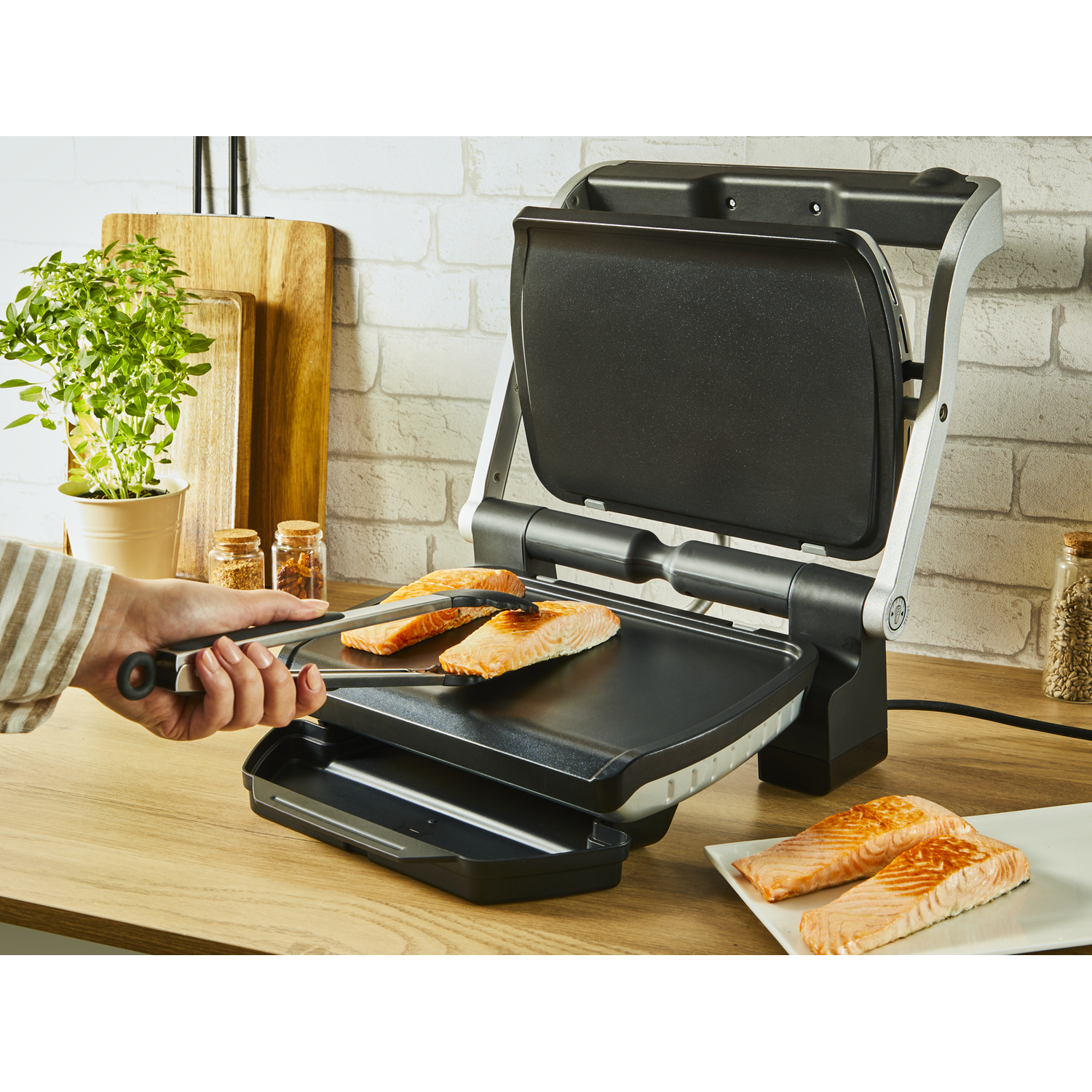 A person uses tongs to flip salmon on a grill.