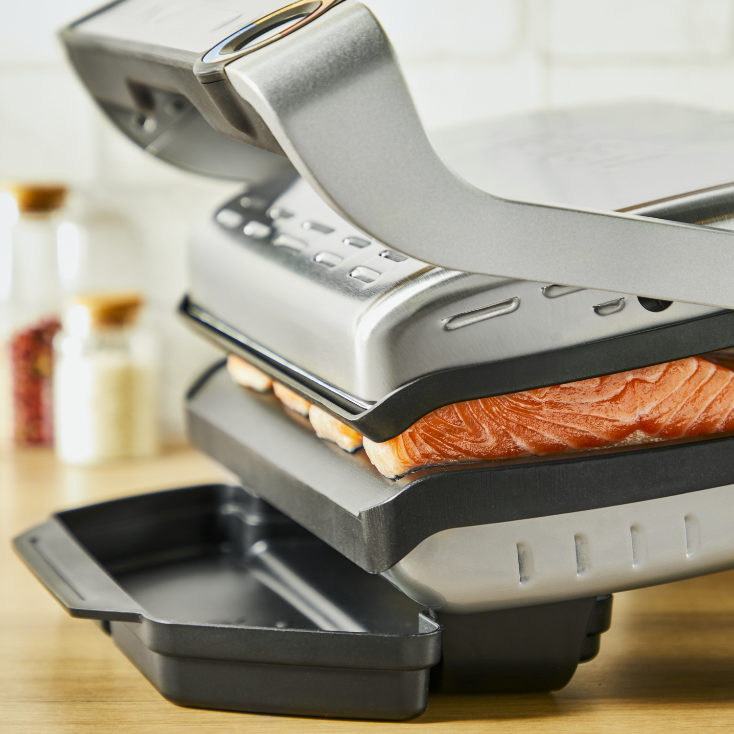 Grill with a salmon fillet, black tray, and blurred background.
