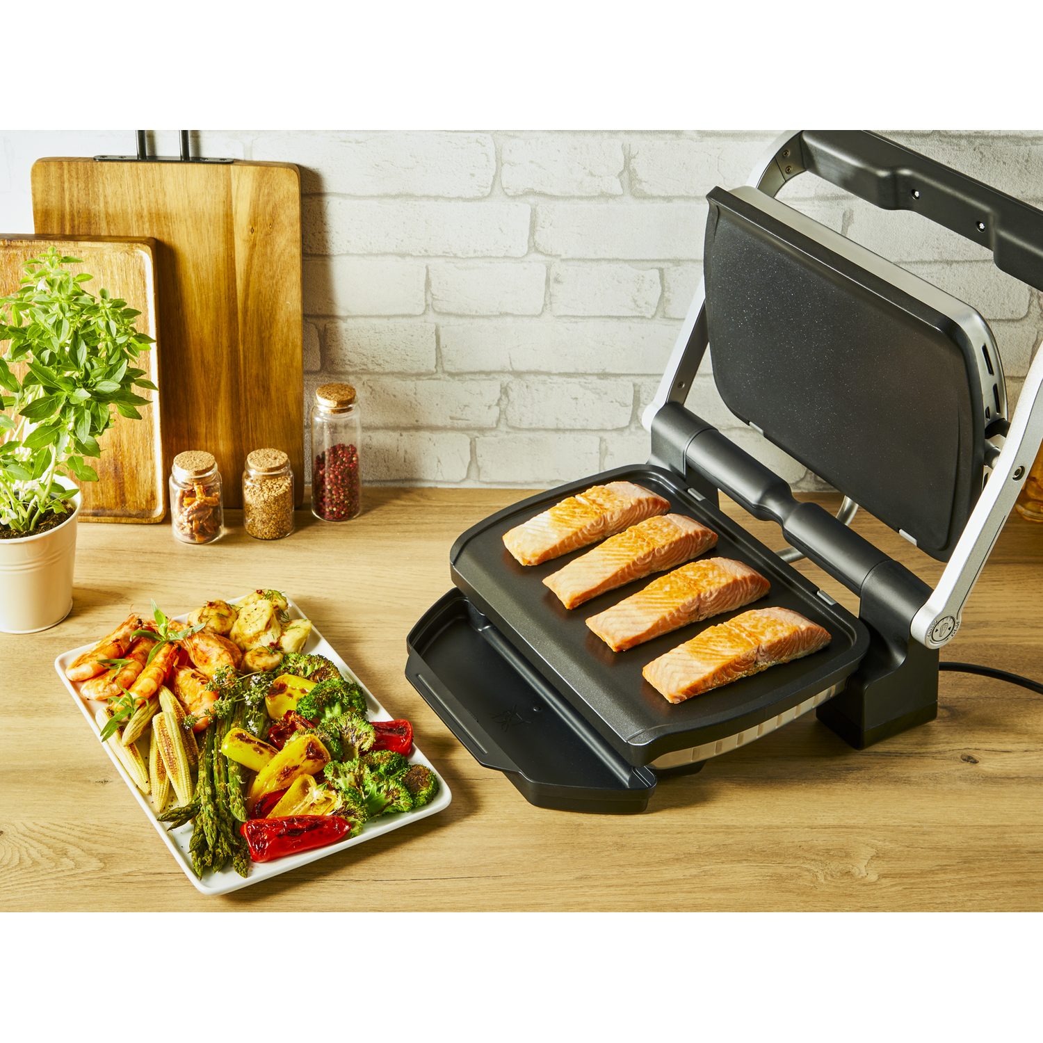 Grilled salmon on a griddle, with a plate of cooked vegetables on the side.