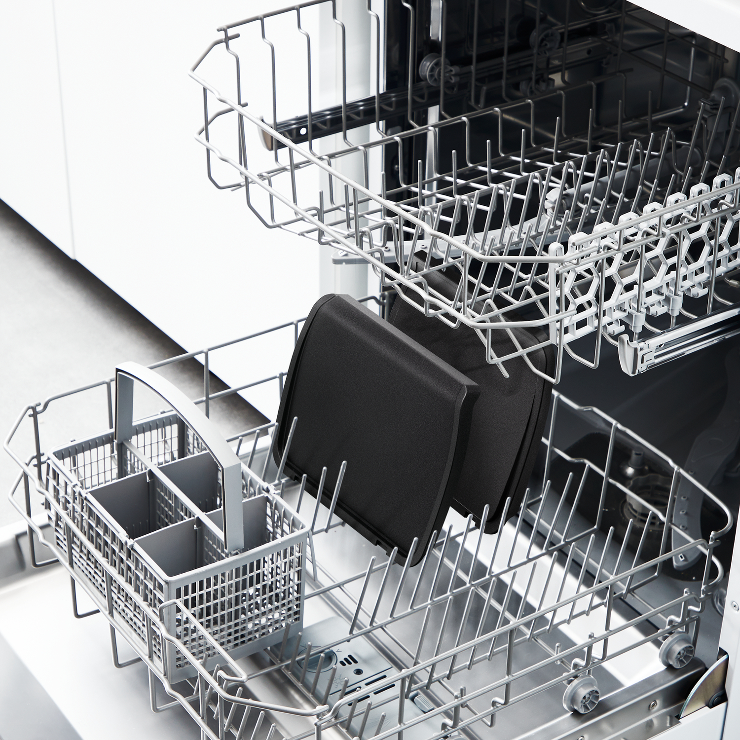 A dishwasher's top rack holds two black square trays. A silverware basket sits in the lower rack.