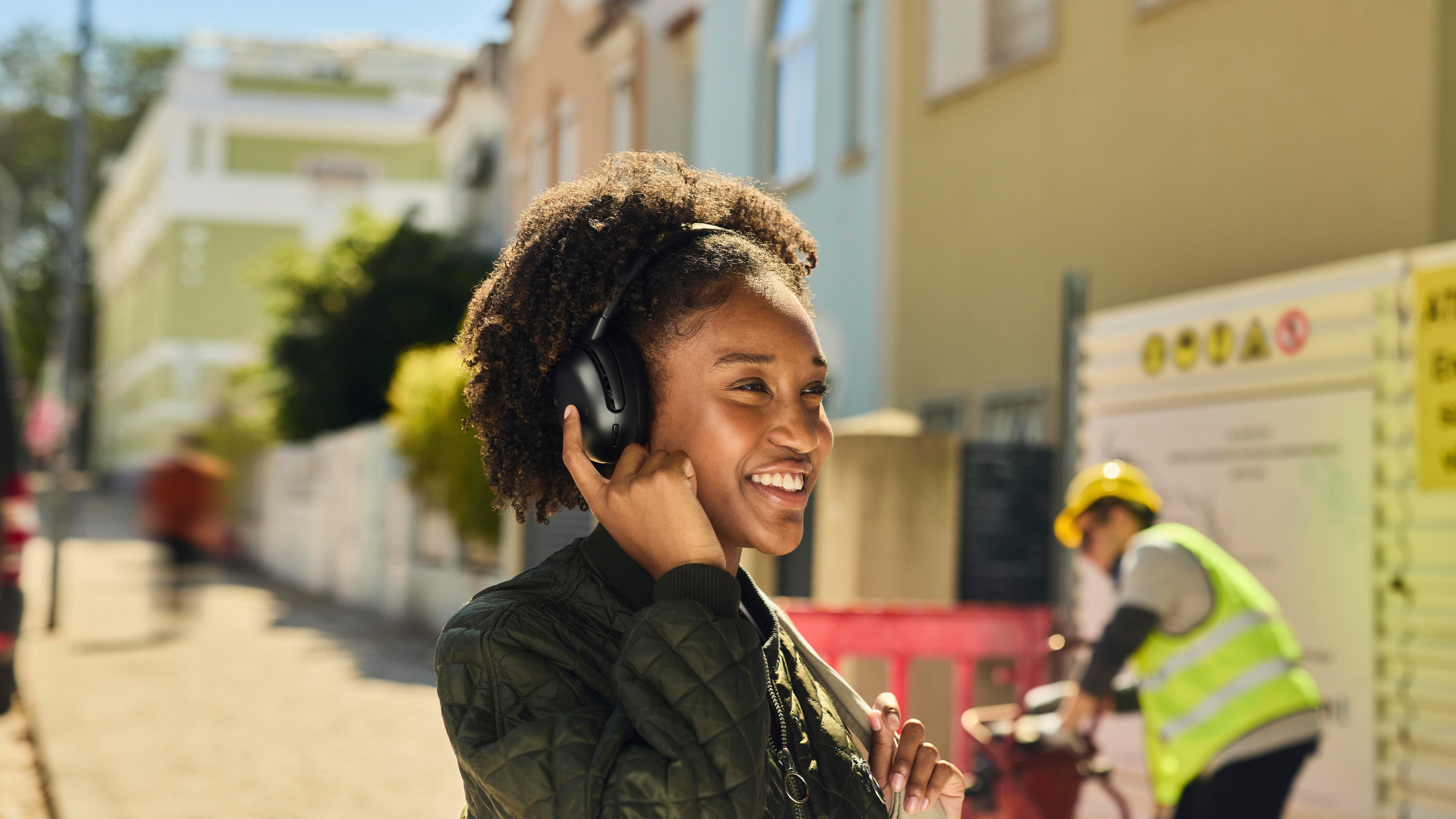 Eine Frau mit Kopfhörern lächelt. Sie steht auf einer Straße mit Bauarbeiten.