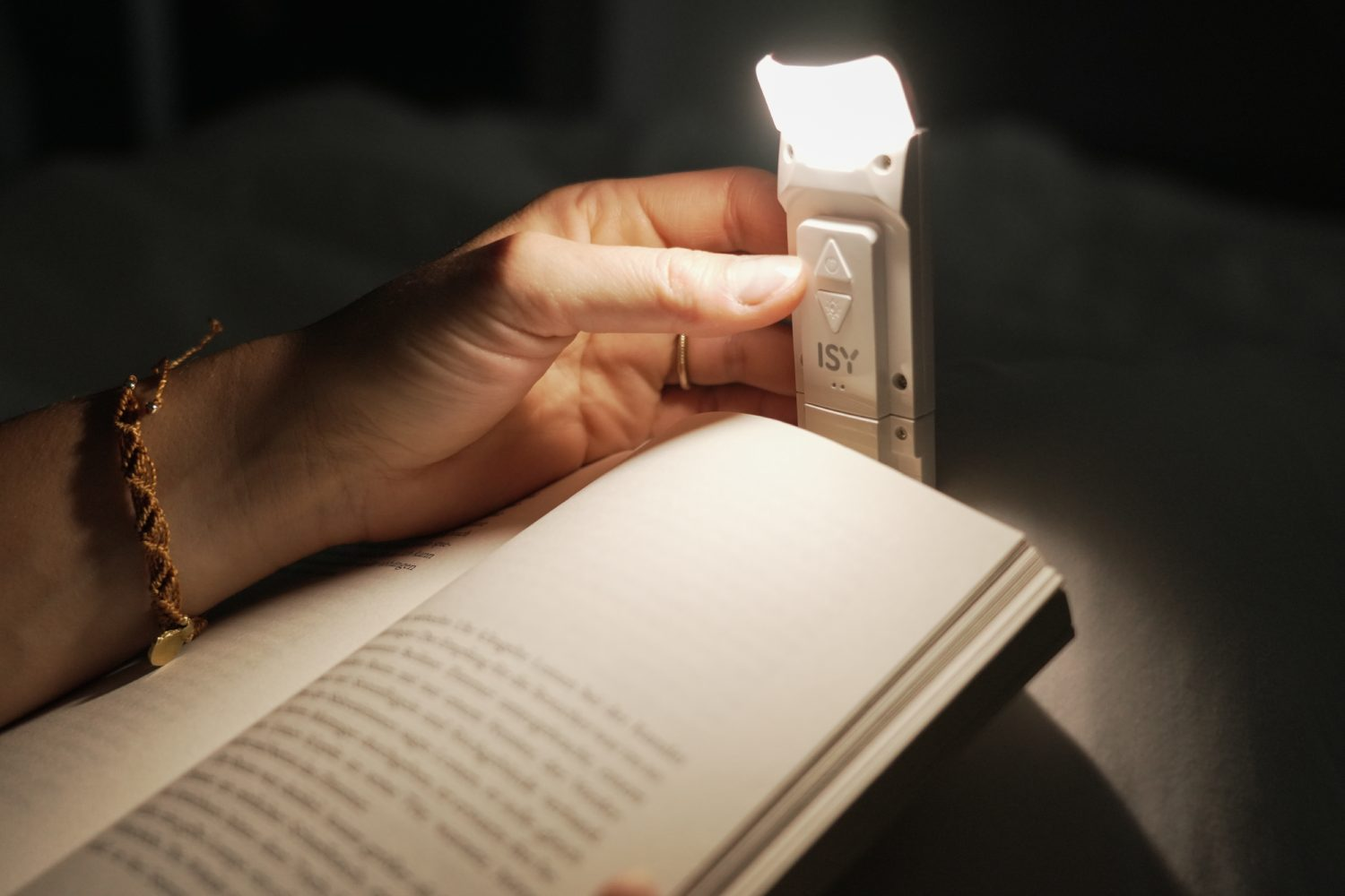 Mano sosteniendo un libro con una luz de lectura. La luz es blanca y pequeña.