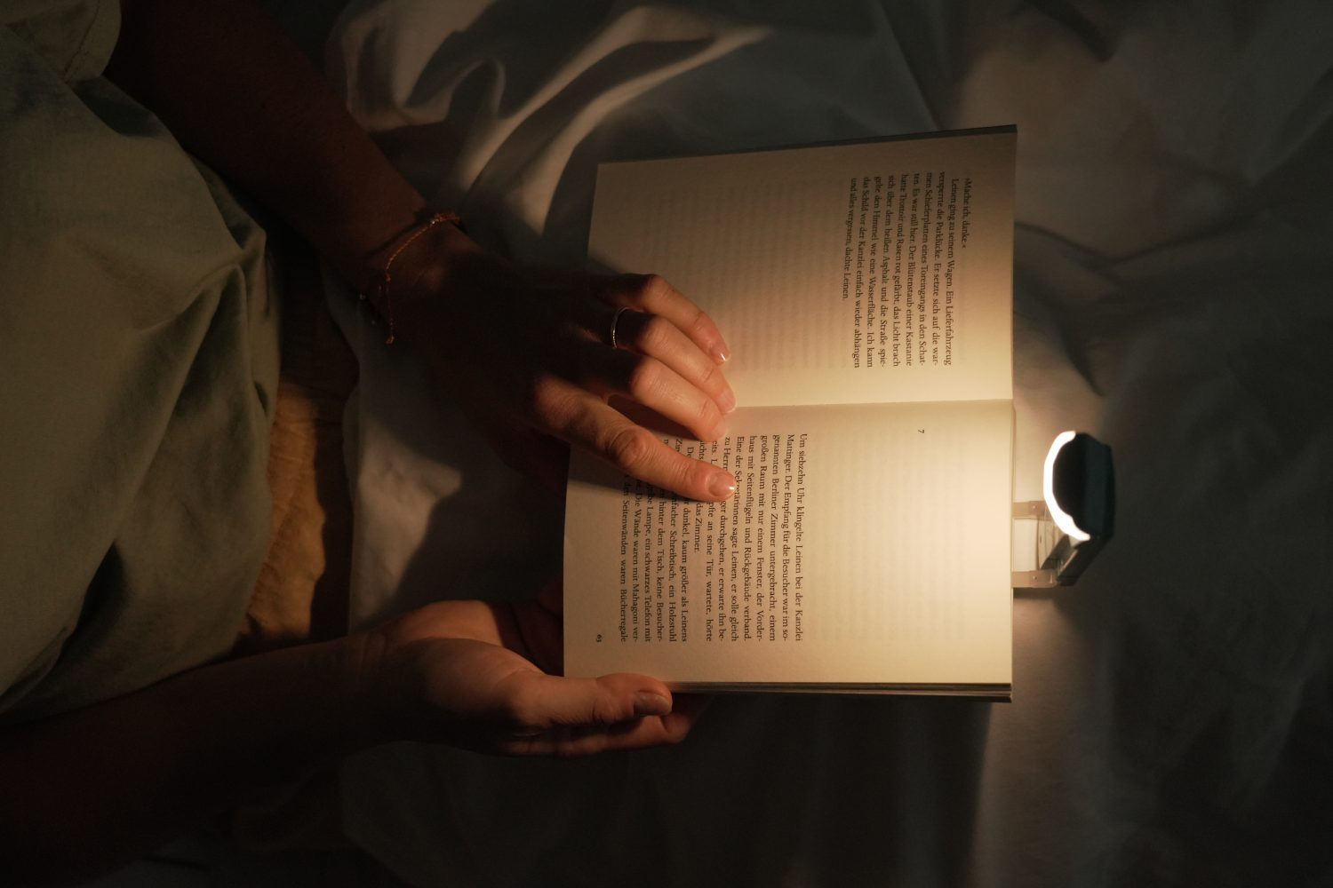 Una persona leyendo un libro en la cama. Una pequeña luz brilla sobre las páginas abiertas. Ángulo bajo.