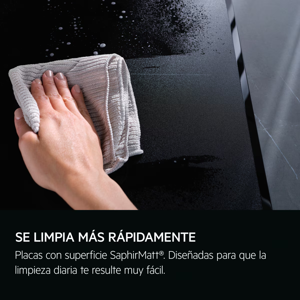 Una mano limpiando una superficie negra con un paño gris.