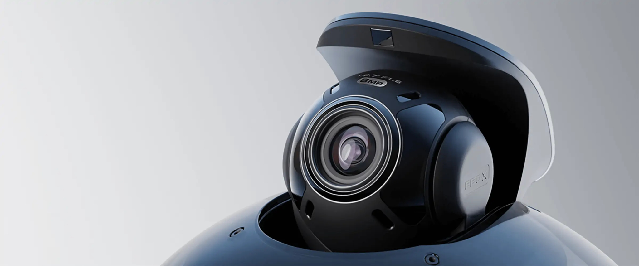 Zbliżenie czarnej kamery z obiektywem. Jest zamontowana na czarnej podstawie. Tło jest jasnoszare.