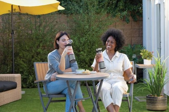 Dwie kobiety w ogrodzie, mieszające napoje, cieszące się słonecznym dniem.