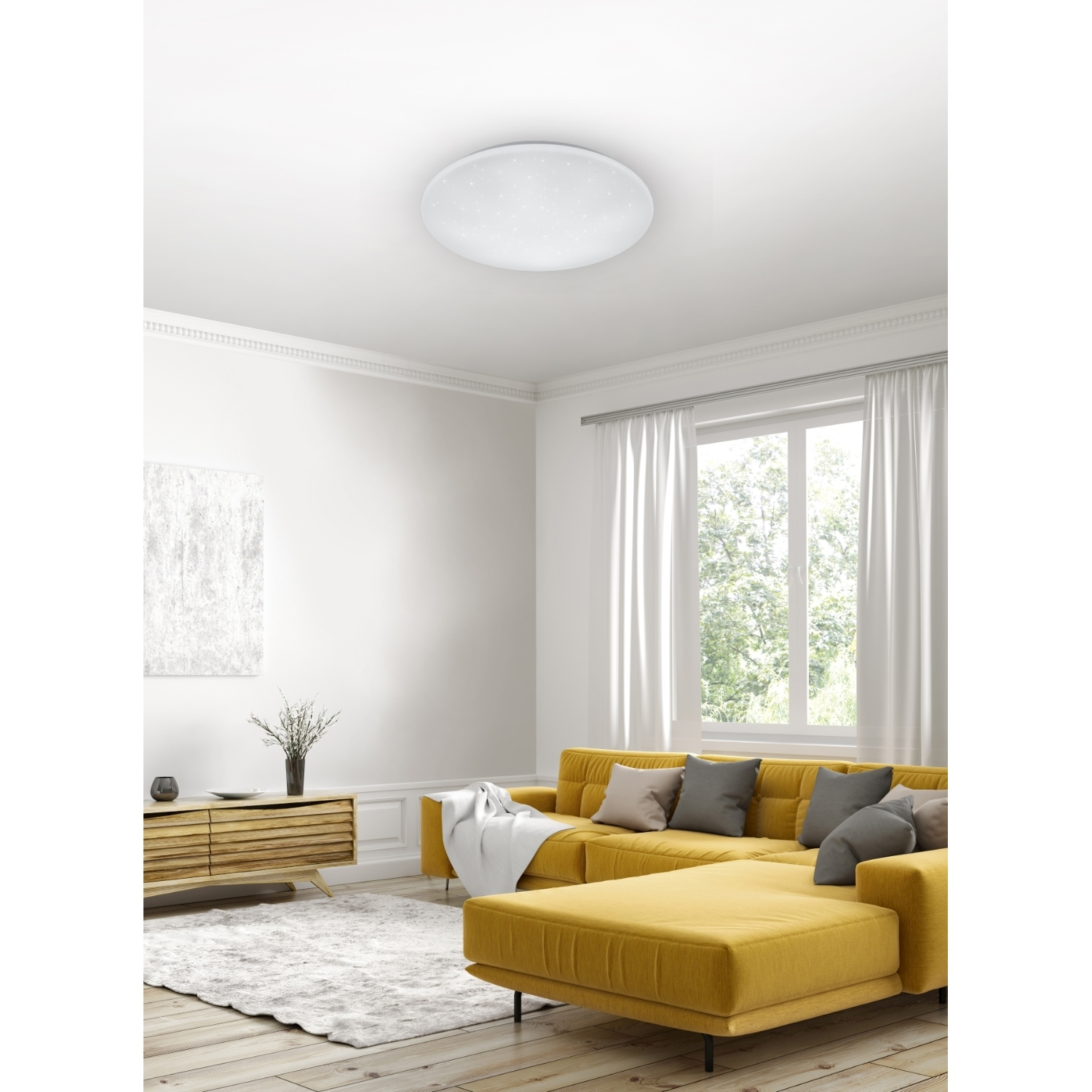 Un soggiorno con divano giallo, tende bianche e un lampada da soffitto.