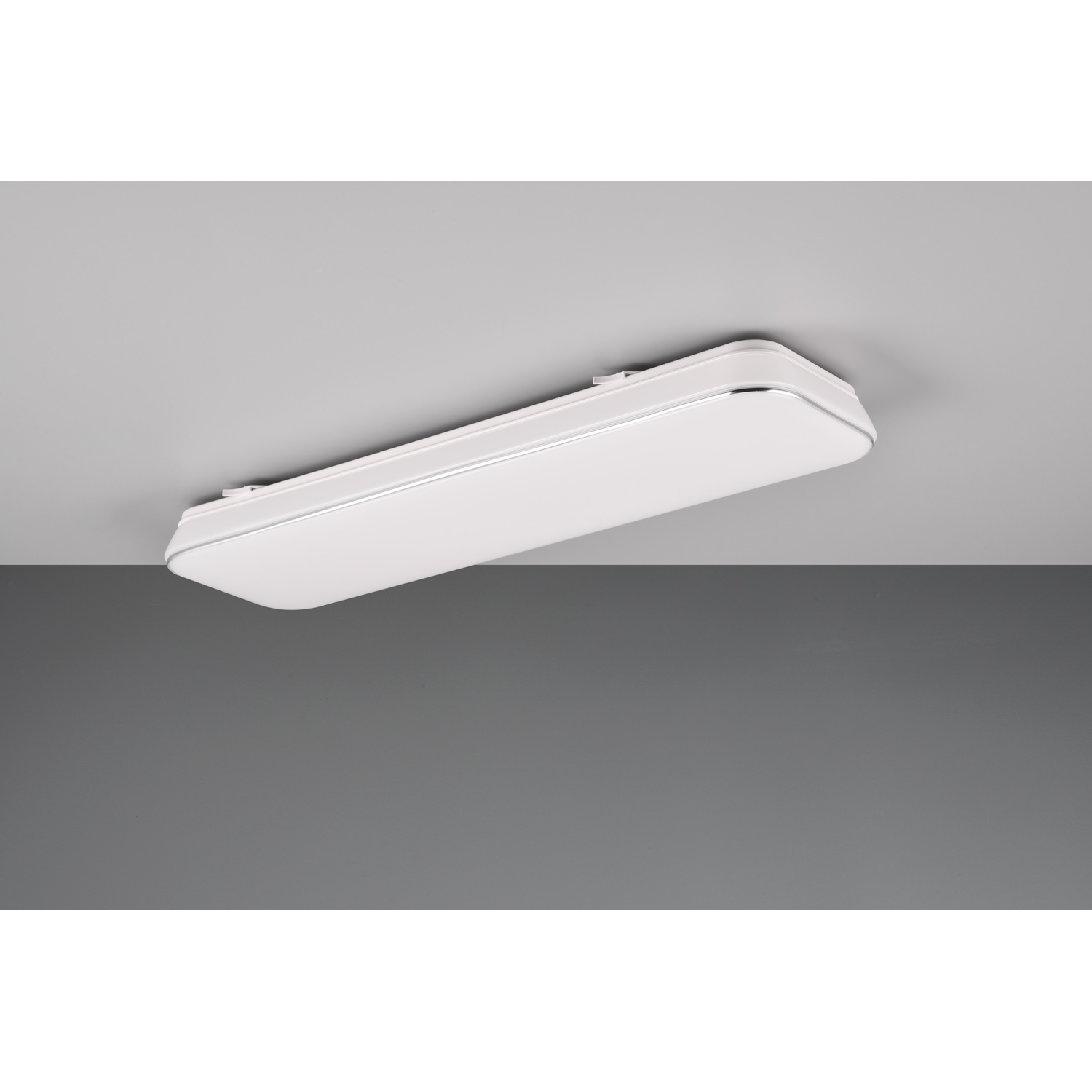 Un lungo apparecchio di illuminazione a soffitto rettangolare bianco contro un soffitto grigio.