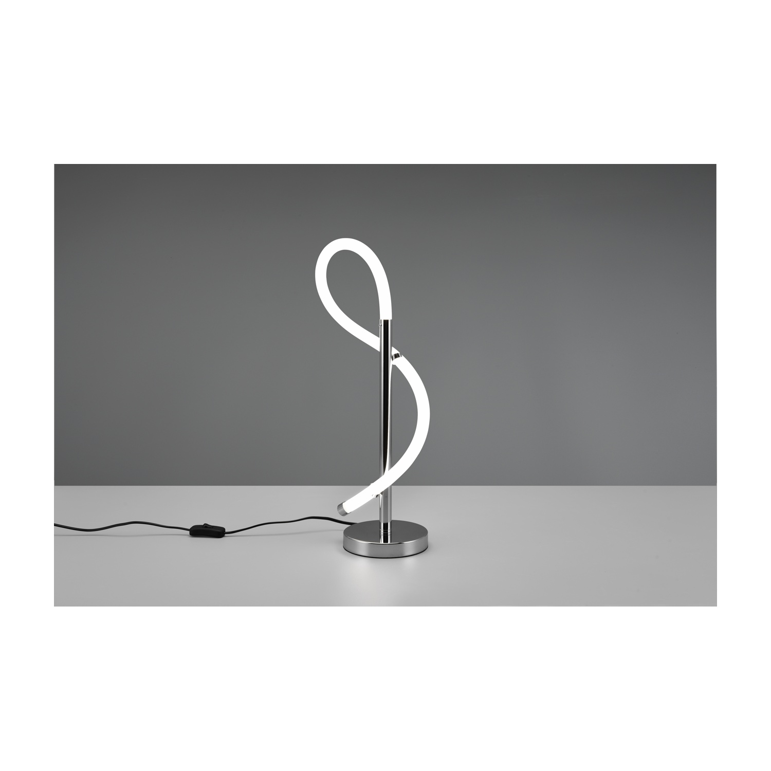 Una lampada da tavolo con base cromata, un'apparecchio luminoso curvo e superficie bianca su sfondo grigio.