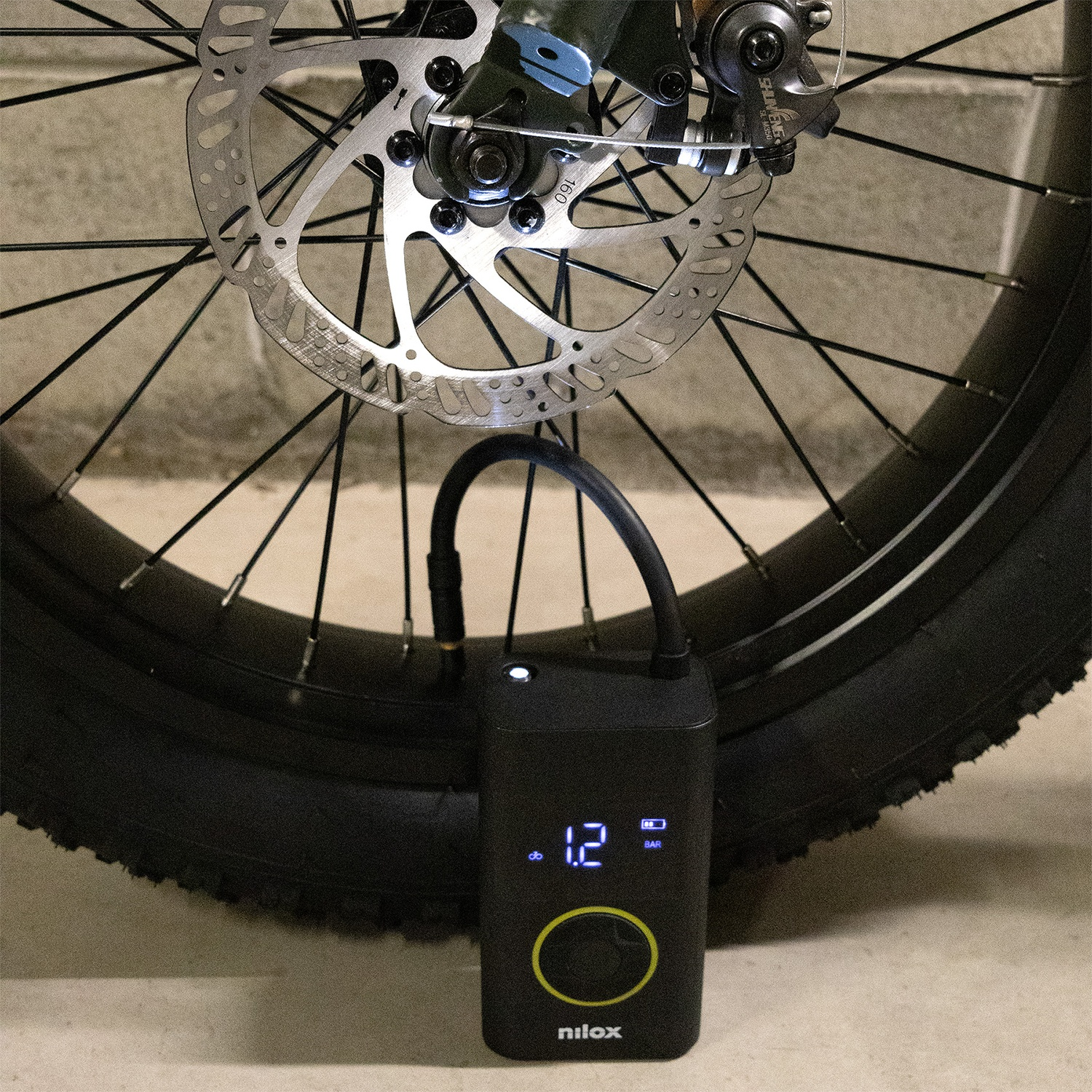 Uno pneumatico nero, una ruota di bicicletta e una pompa Nilox nera con display digitale.