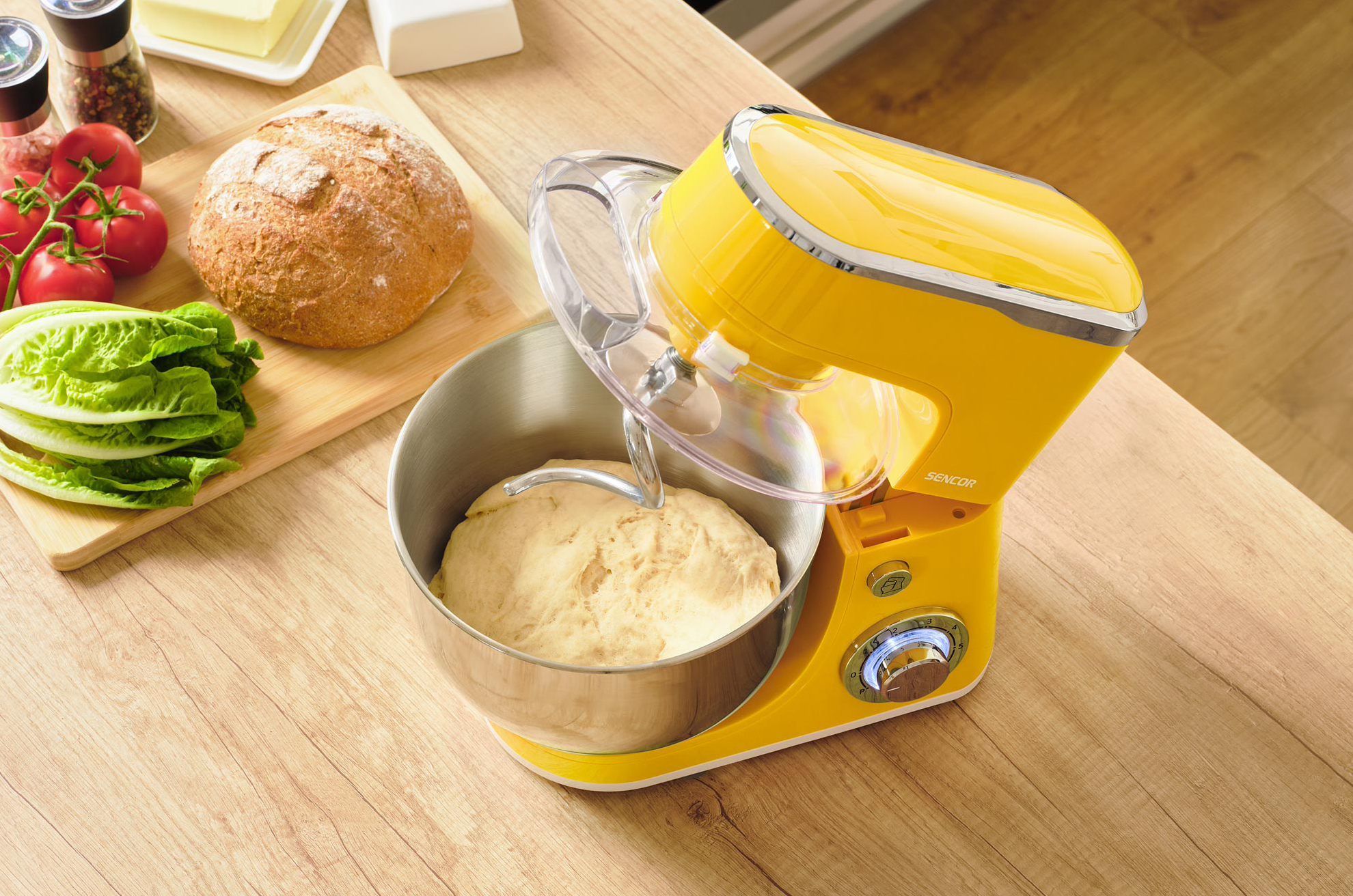 Sárga konyhai mixer tésztával, faasztalon. Kenyér és hozzávalók a közelben.