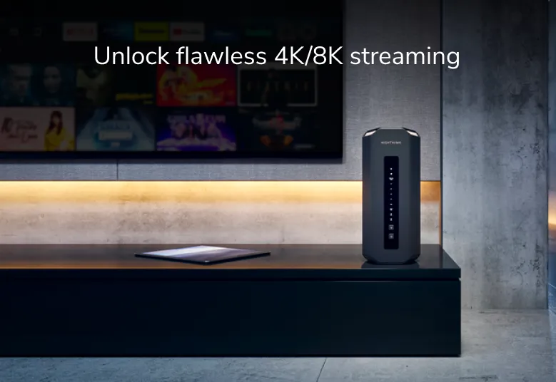 Ein schwarzer Router. Ein Tablet liegt vor einem Fernseher auf der Oberfläche.