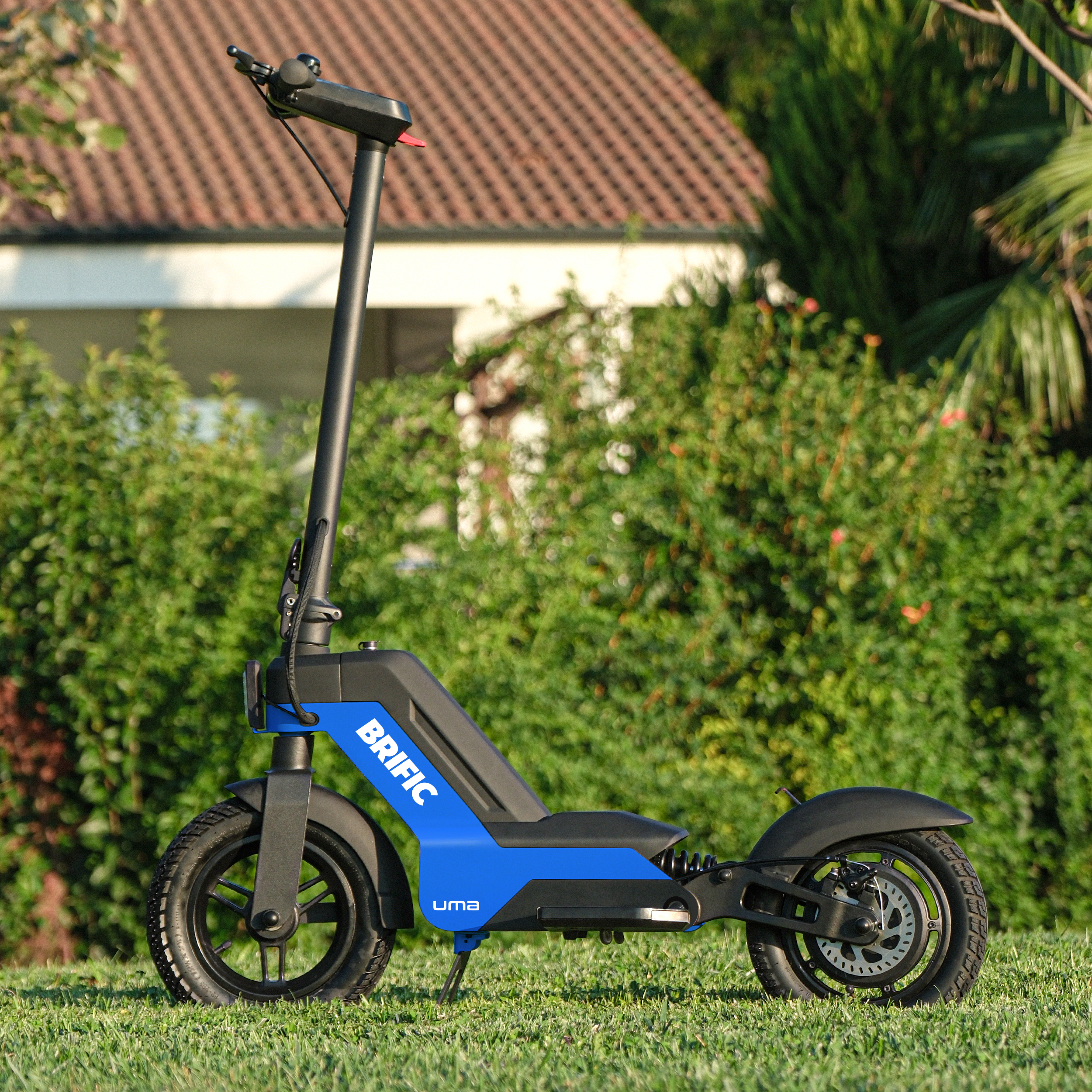 Mavi ve siyah elektrikli scooter yeşil çim üzerinde, marka BRIFIC. Arka planda bir ev.