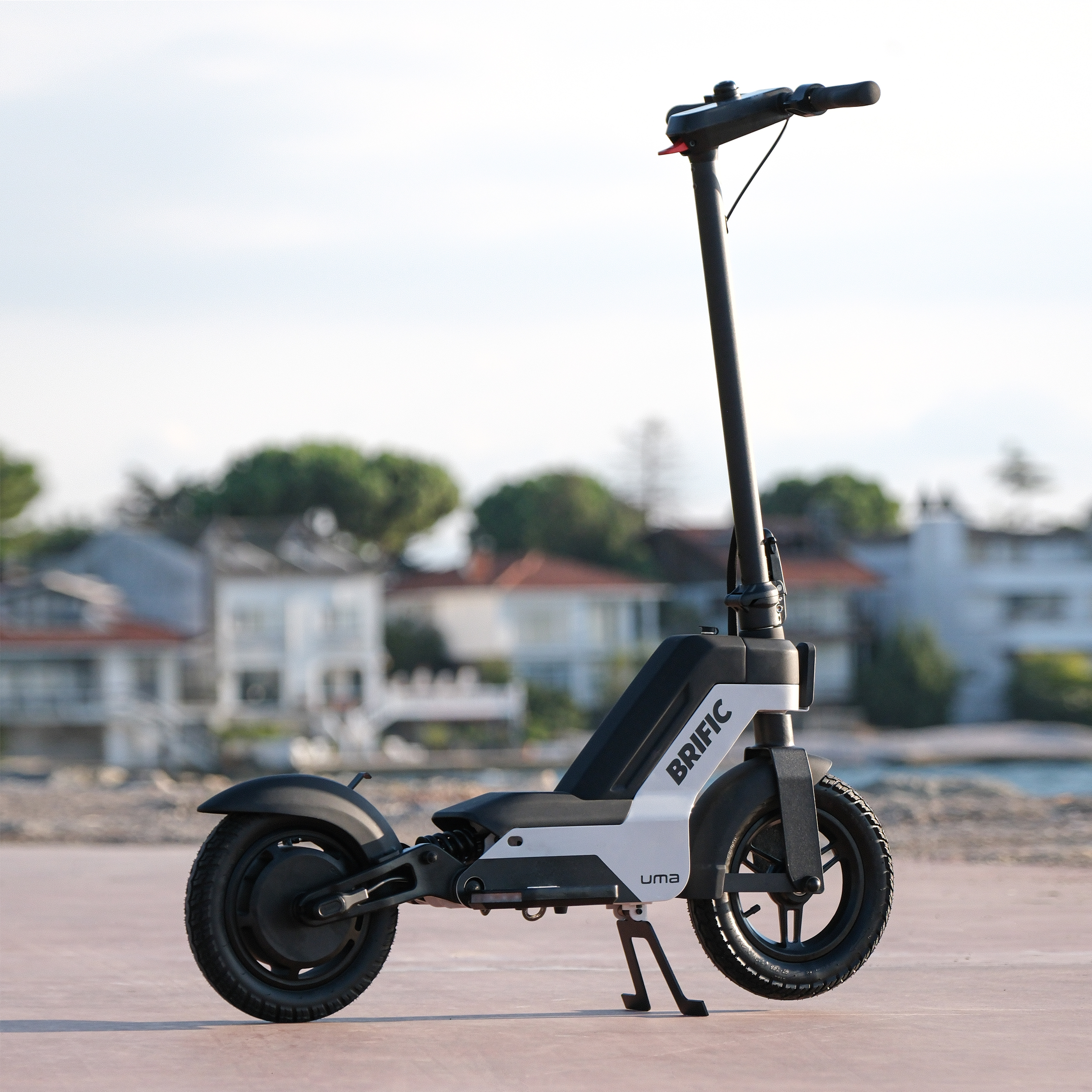 Deniz kenarında beton bir yüzeyde siyah beyaz bir elektrikli scooter, arka planda berrak gökyüzü.