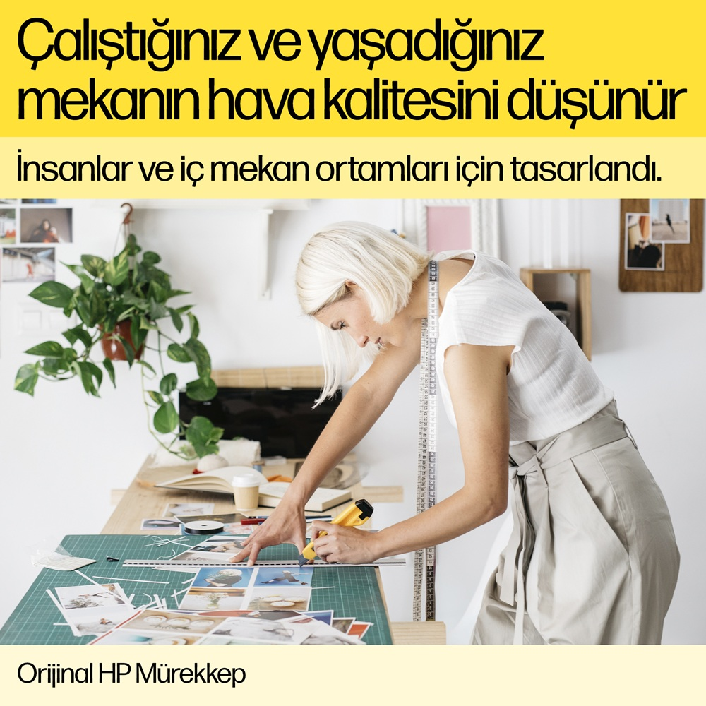 Bir kadın bir masada çalışıyor, bir cetvel ve sarı bir kesici ile kağıda çizim yapıyor.