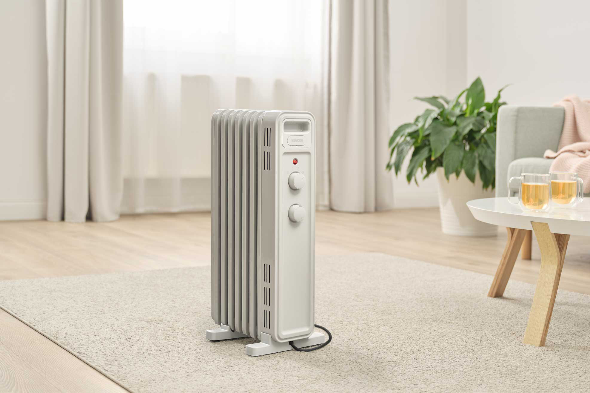 Fehér és szürke olajradiátor a nappaliban, egy ablak közelében, asztallal.