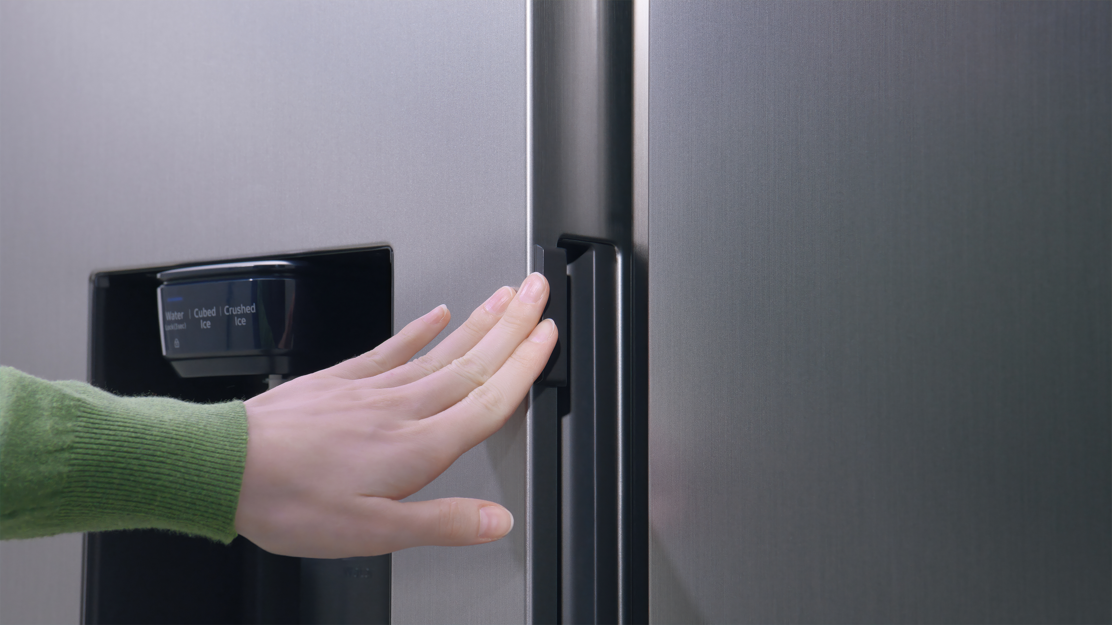 Eine Hand berührt eine Kühlschranktür. Die Tür hat einen Wasser- und Eisspender.