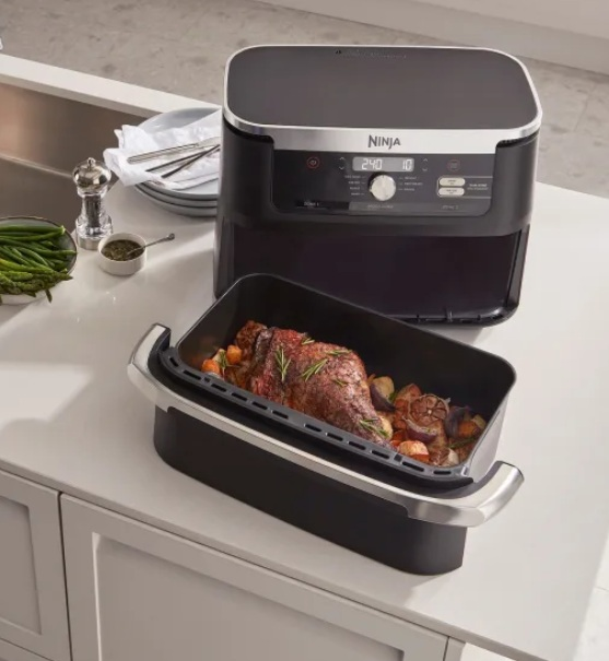 Czarna i srebrna frytkownica beztłuszczowa Ninja z pojemnikiem do gotowania z jedzeniem, na białym blacie.