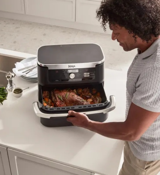 Mężczyzna otwiera czarną frytkownicę powietrzną Ninja z pieczonym jedzeniem w środku.