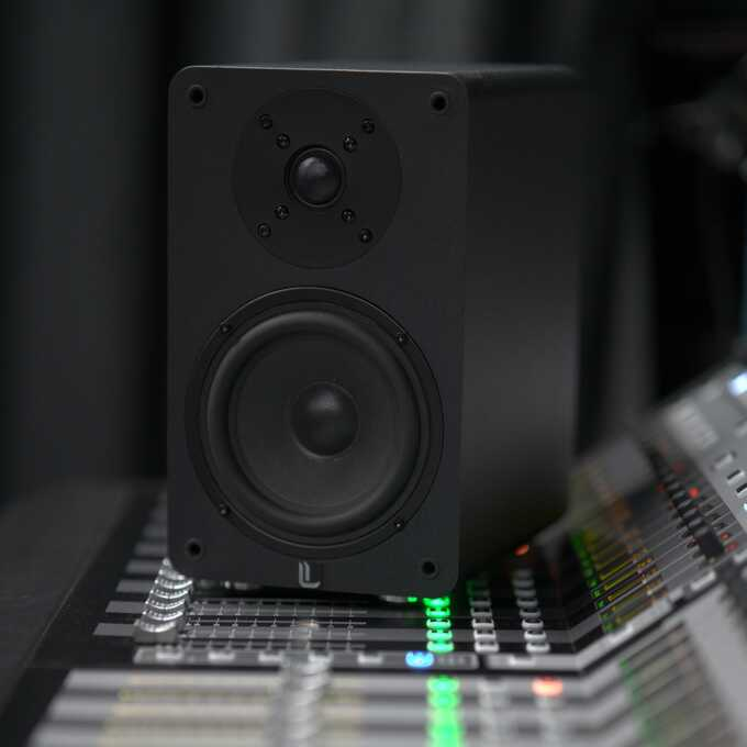 Czarny głośnik na stole w pobliżu miksera dźwięku.