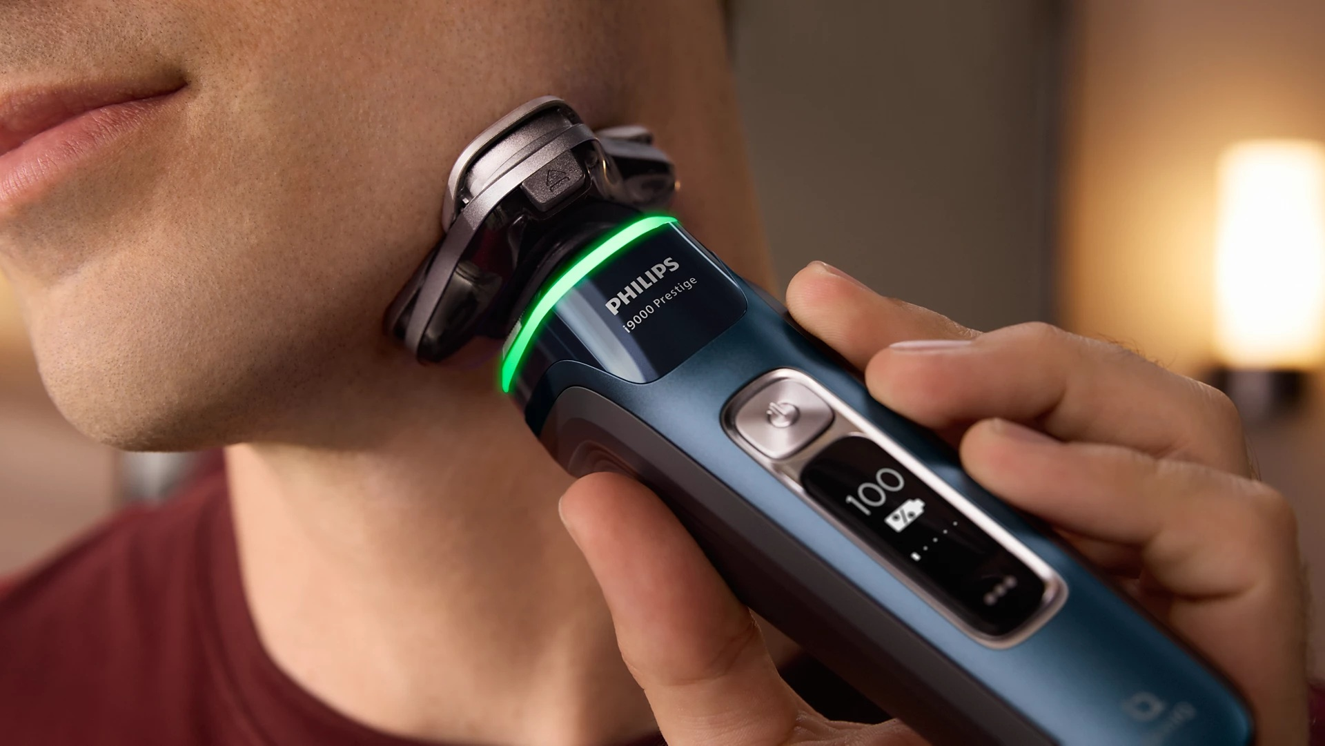 Mężczyzna goli twarz golarką elektryczną. Świeci zielone światło. Tło jest rozmyte.