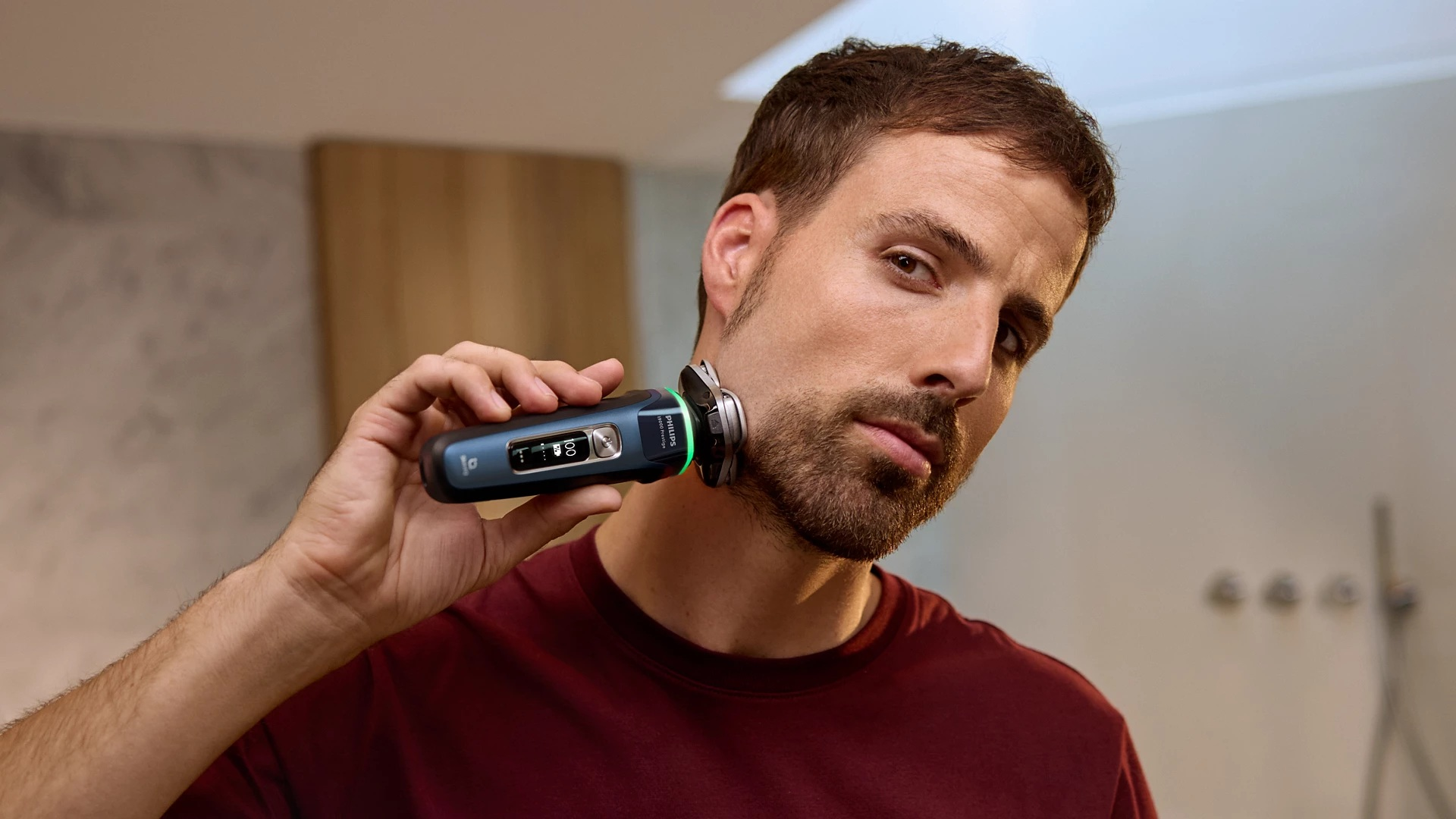 Mężczyzna goli brodę golarką elektryczną. Tło to łazienka.