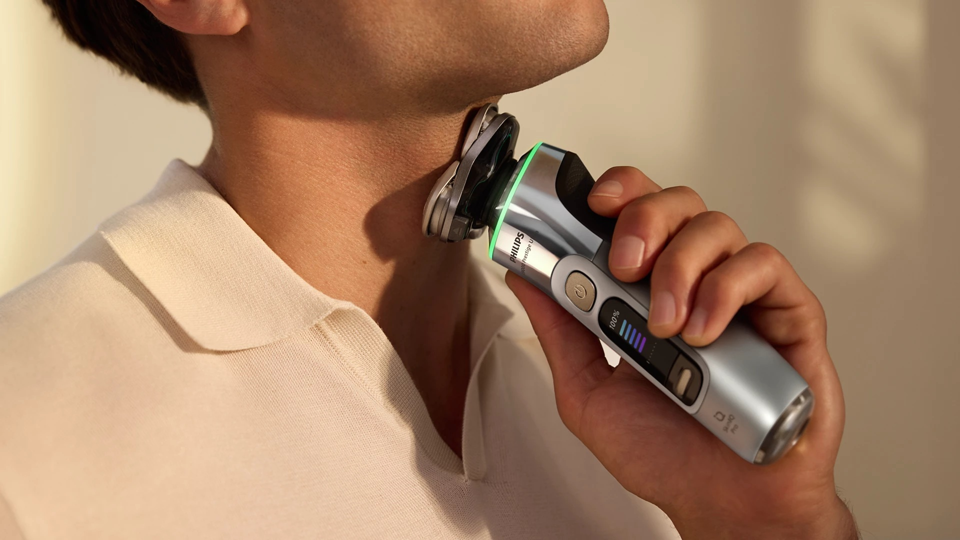 Mężczyzna goli się srebrną golarką elektryczną. Golarka jest blisko szyi.