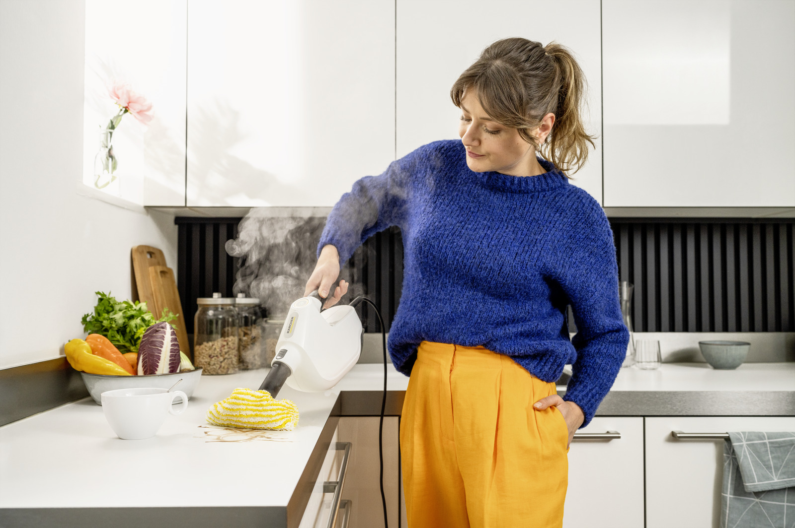 Kobieta czyszcząca blat za pomocą białego urządzenia parowego.
