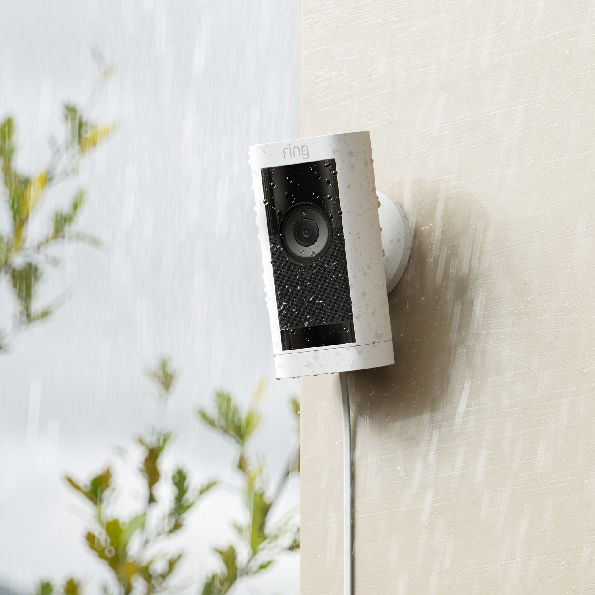 Eine weiße Ring-Sicherheitskamera ist an einer Wand montiert. Wassertropfen sind vom Regen sichtbar.