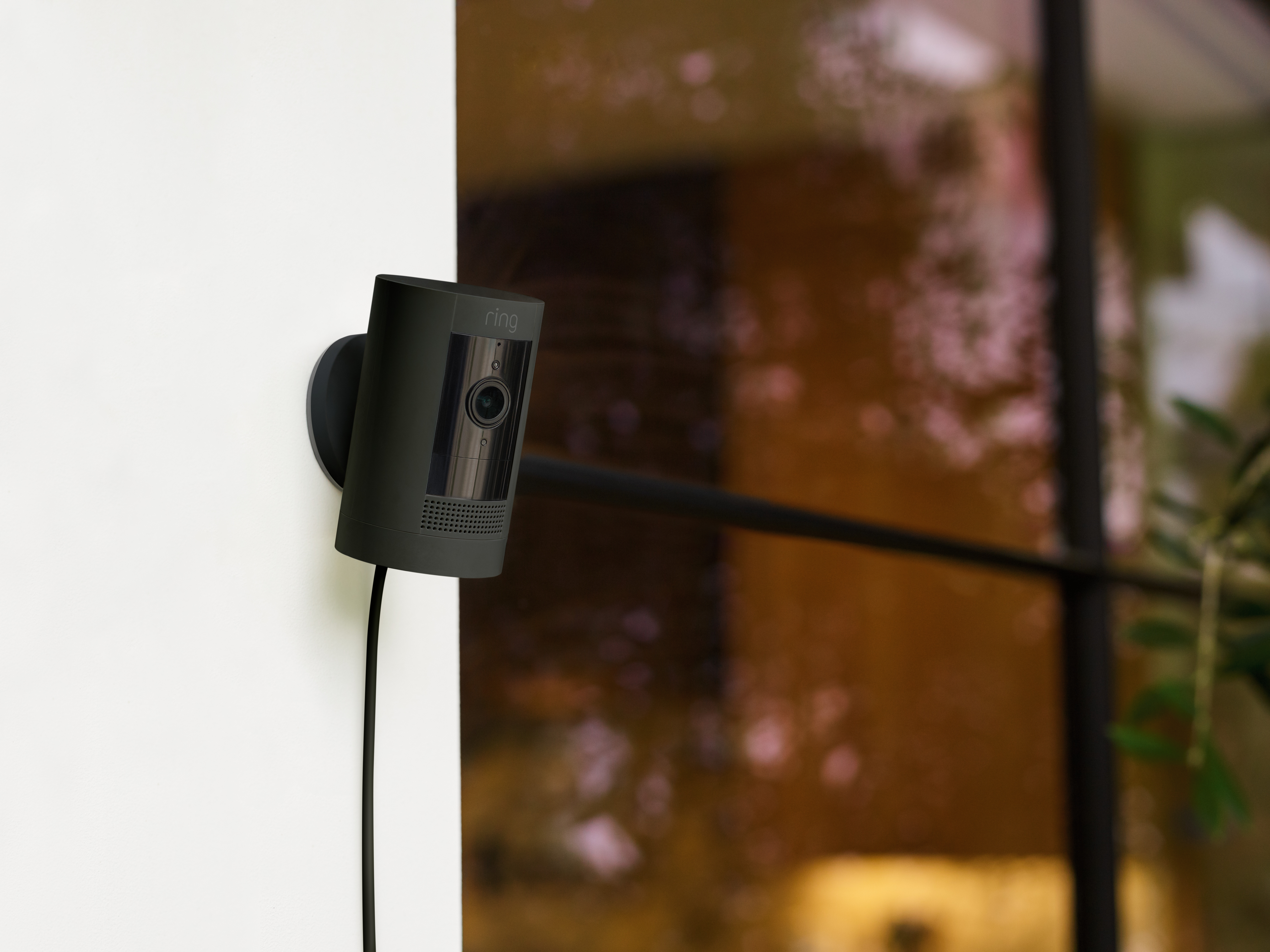Schwarze Überwachungskamera an einer weißen Wand befestigt. Sie ist auf ein Fenster und einen schwarzen Griff gerichtet.