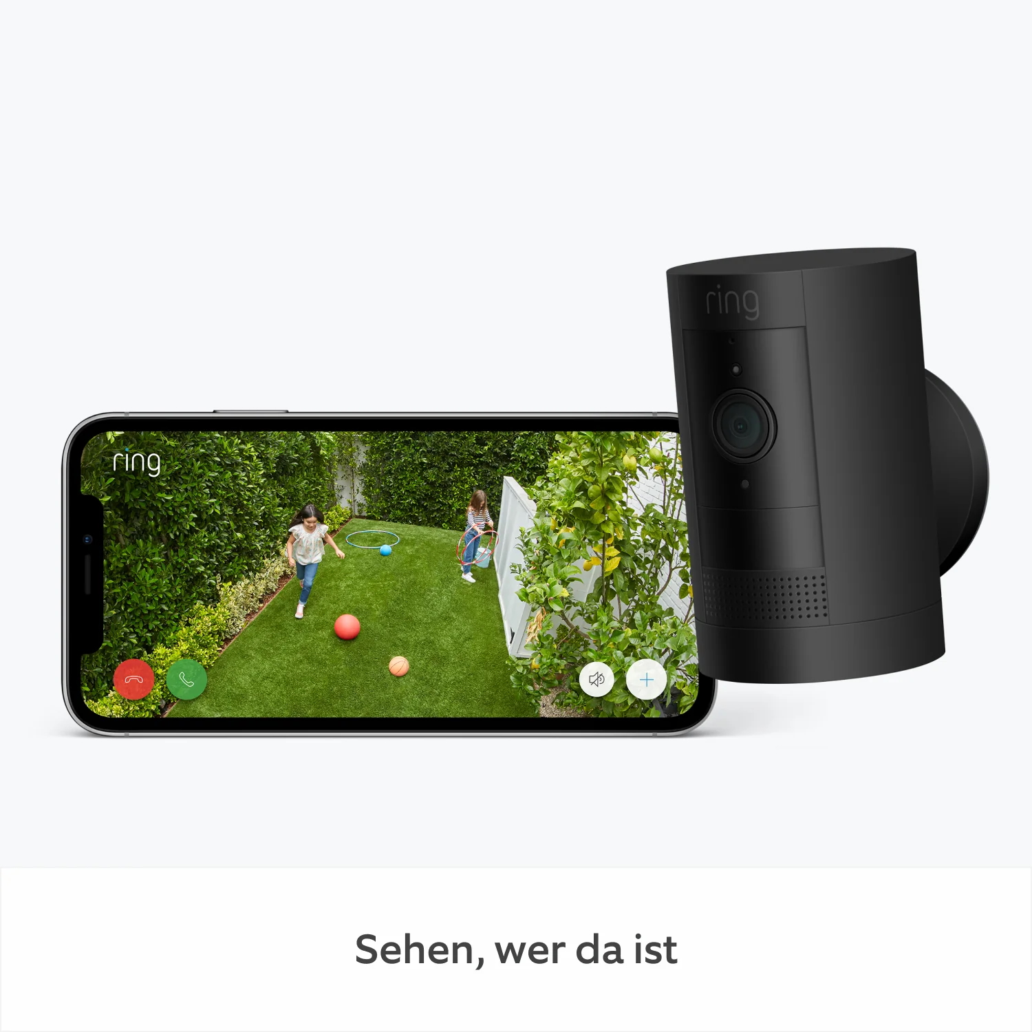 Ein Smartphone zeigt Kinder beim Spielen in einem Garten, mit einer Ring-Sicherheitskamera in der Nähe.