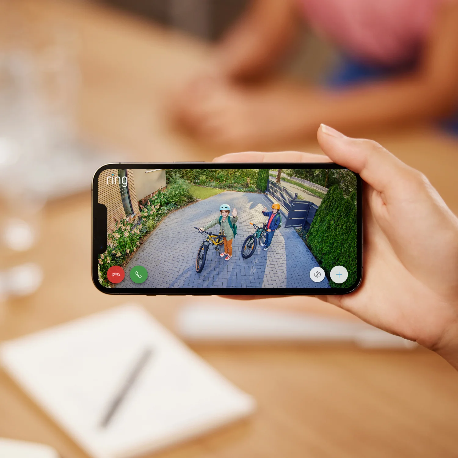 Eine Hand, die ein Telefon hält, zeigt zwei Kinder auf Fahrrädern, Ansicht von einer Ring-Türklingelkamera.