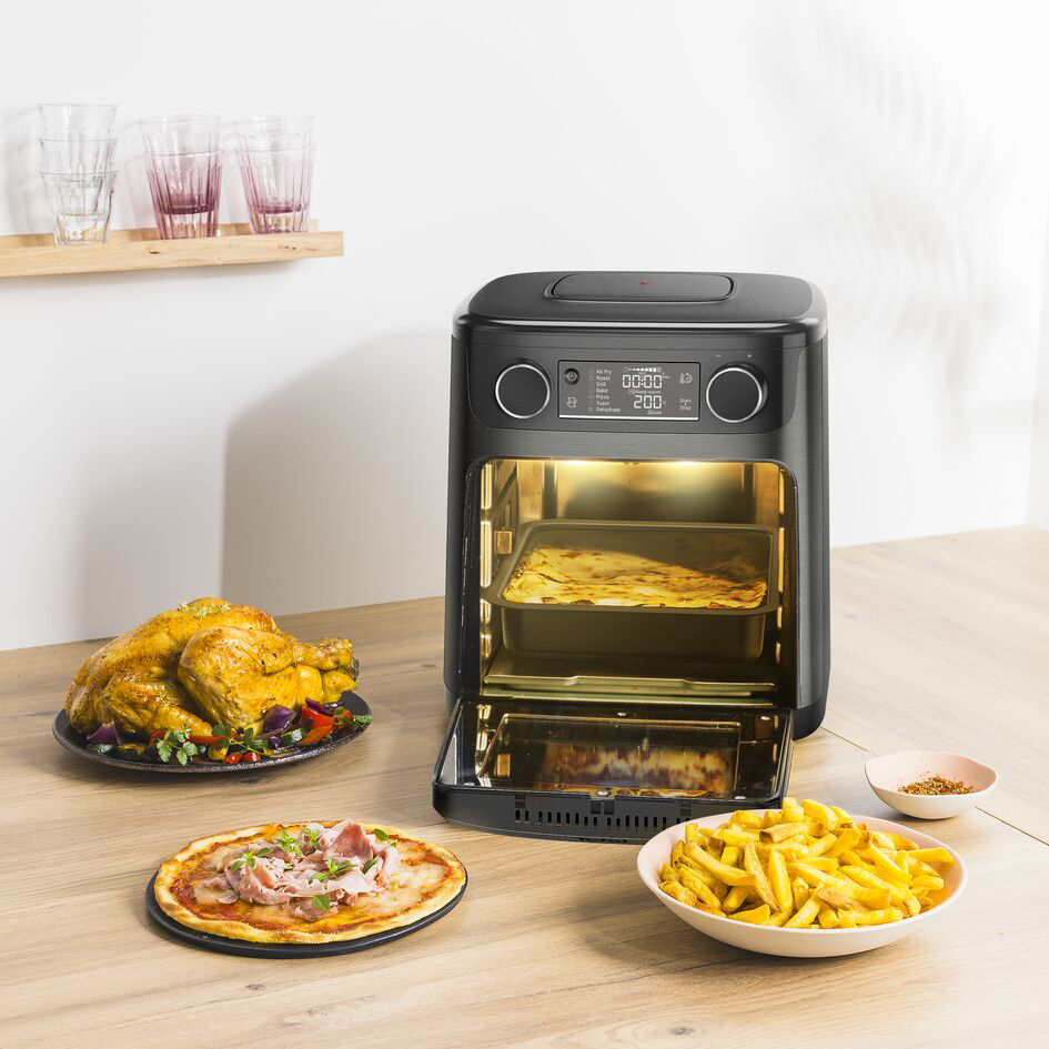 Egy nyitott légsütő főtt étellel az asztalon: pizza, sült krumpli és csirke.