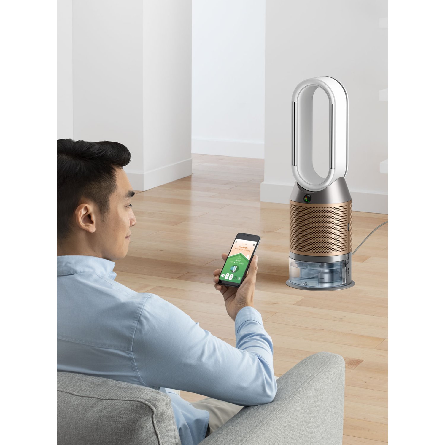 Man using a smartphone controlling a white and gold air purifier, sitting on a couch.