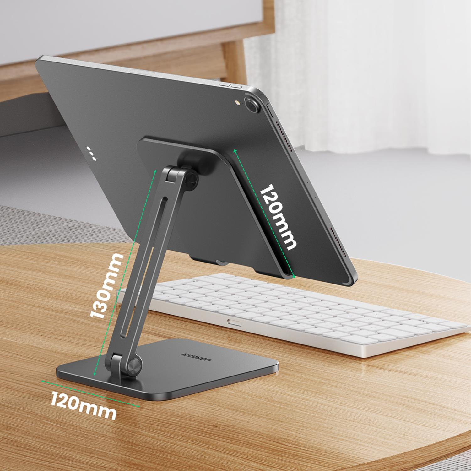 Gümüş bir stand üzerinde tablet, bir kolla destekleniyor, ahşap bir masa üzerinde klavye.