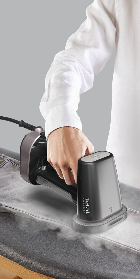 Egy személy Tefal Pure Force vasalóval gőzöli a farmert, szürke háttér, fehér ing.