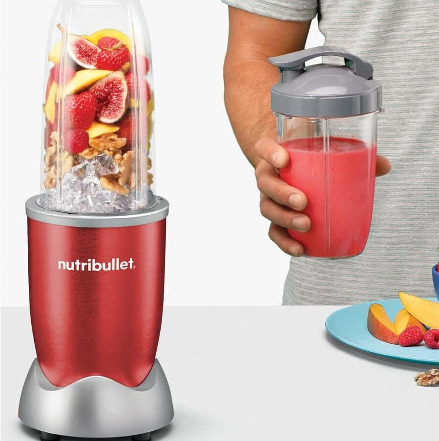 Roter Nutribullet-Mixer mit Früchten und Eis, Person hält Smoothie-Becher.