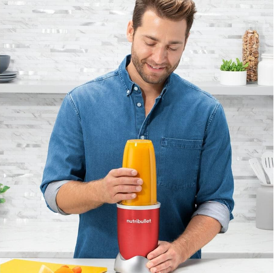 Mann hält einen Nutribullet mit orangener Flüssigkeit in einer Küche.