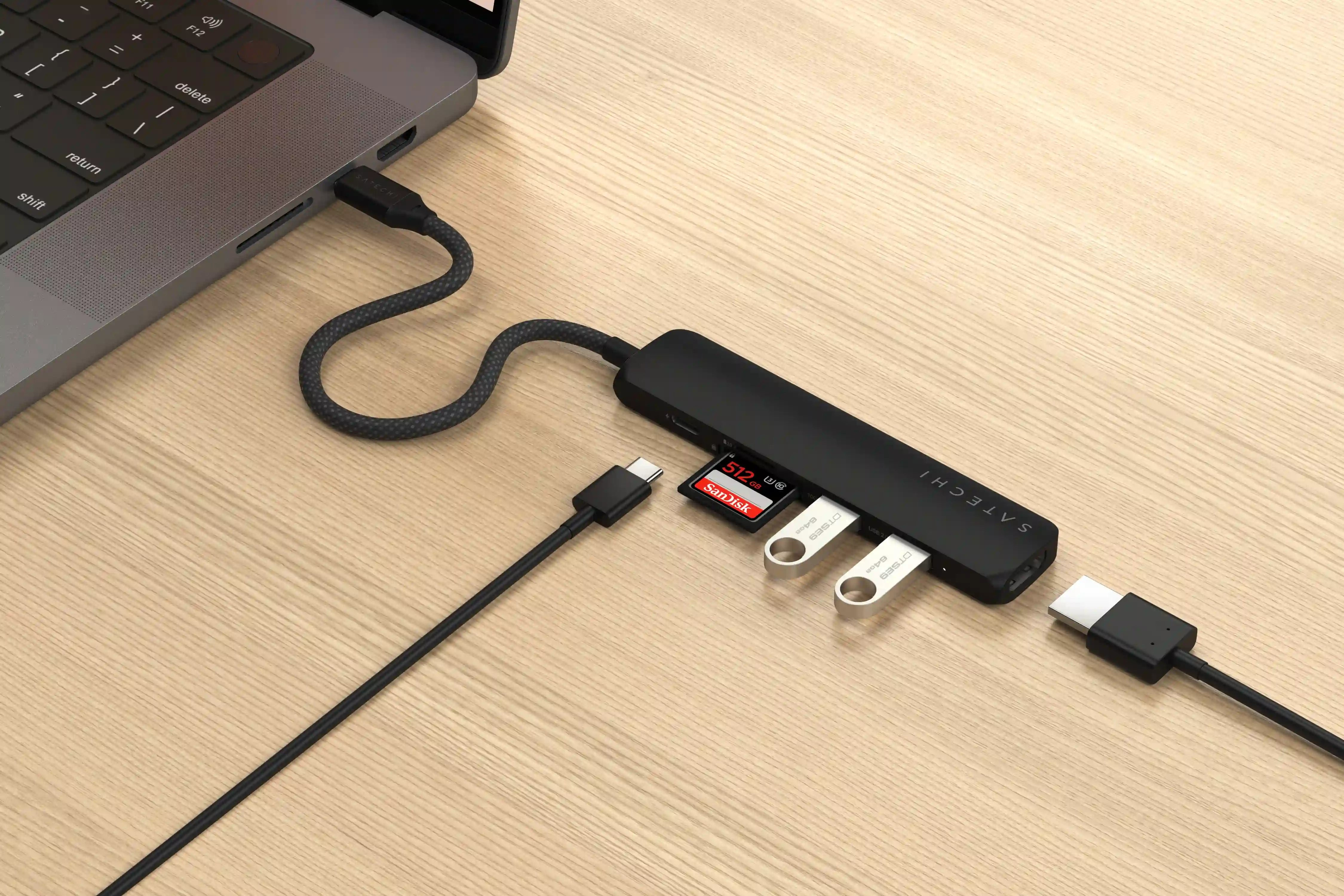 Ein Laptop, der an einen schwarzen Hub mit USB-, SD-Karten- und USB-C-Anschlüssen und einem USB-C-Kabel angeschlossen ist.