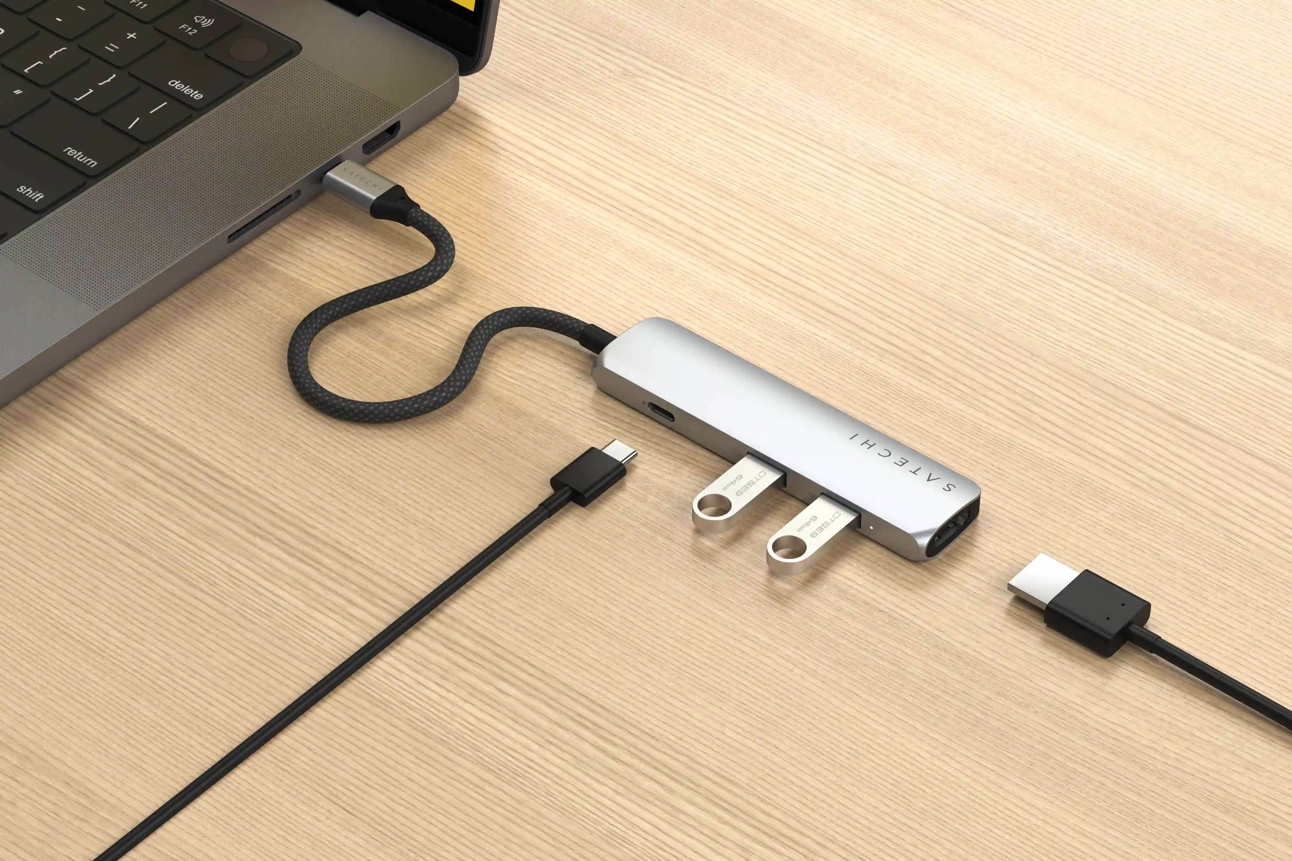 Laptop mit silbernem Hub verbunden. USB-Laufwerke und Ladekabel angeschlossen. Holz Hintergrund.
