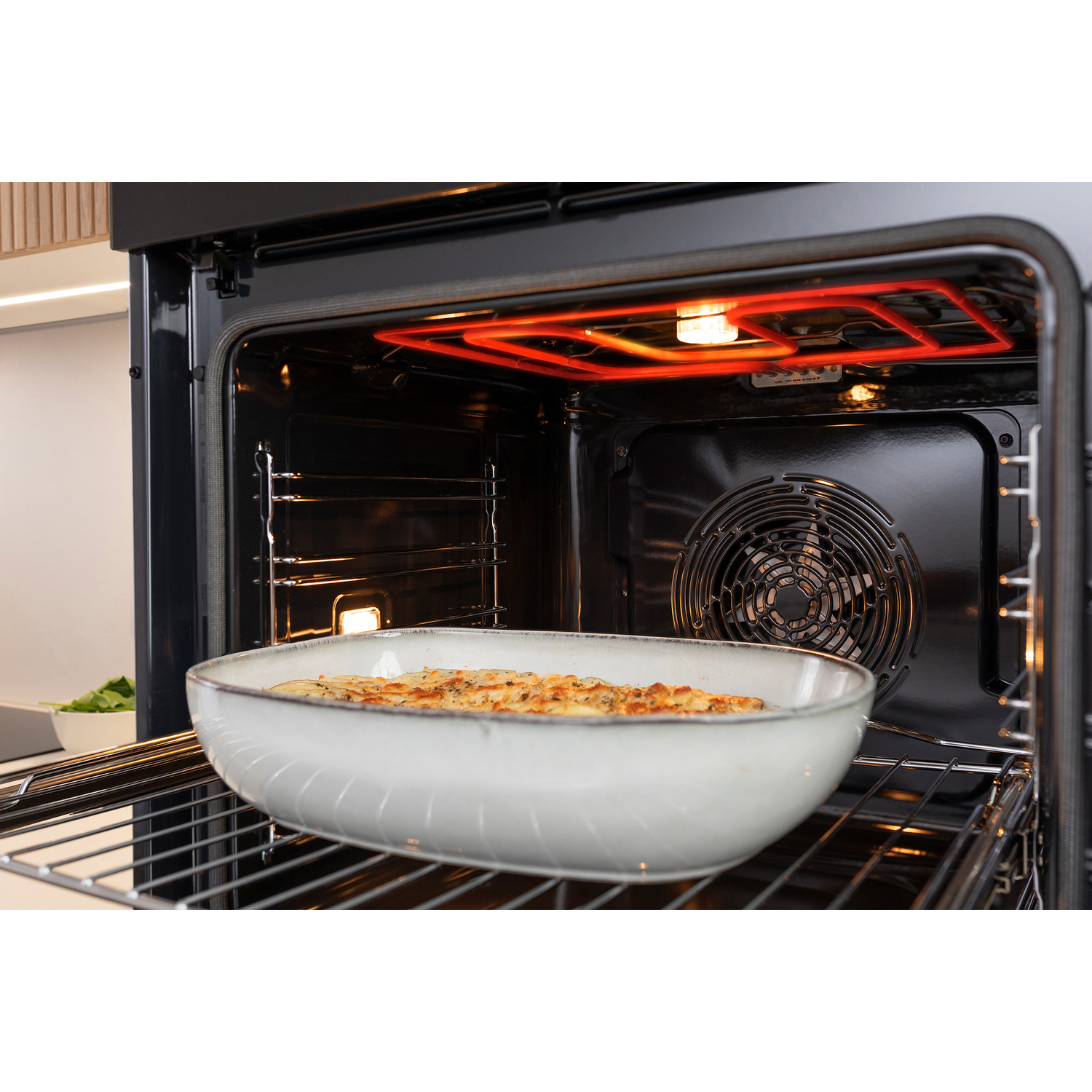 Oven interior shows a dish with baked food. Red heating element glows above. Fan in the back. Oven door open.