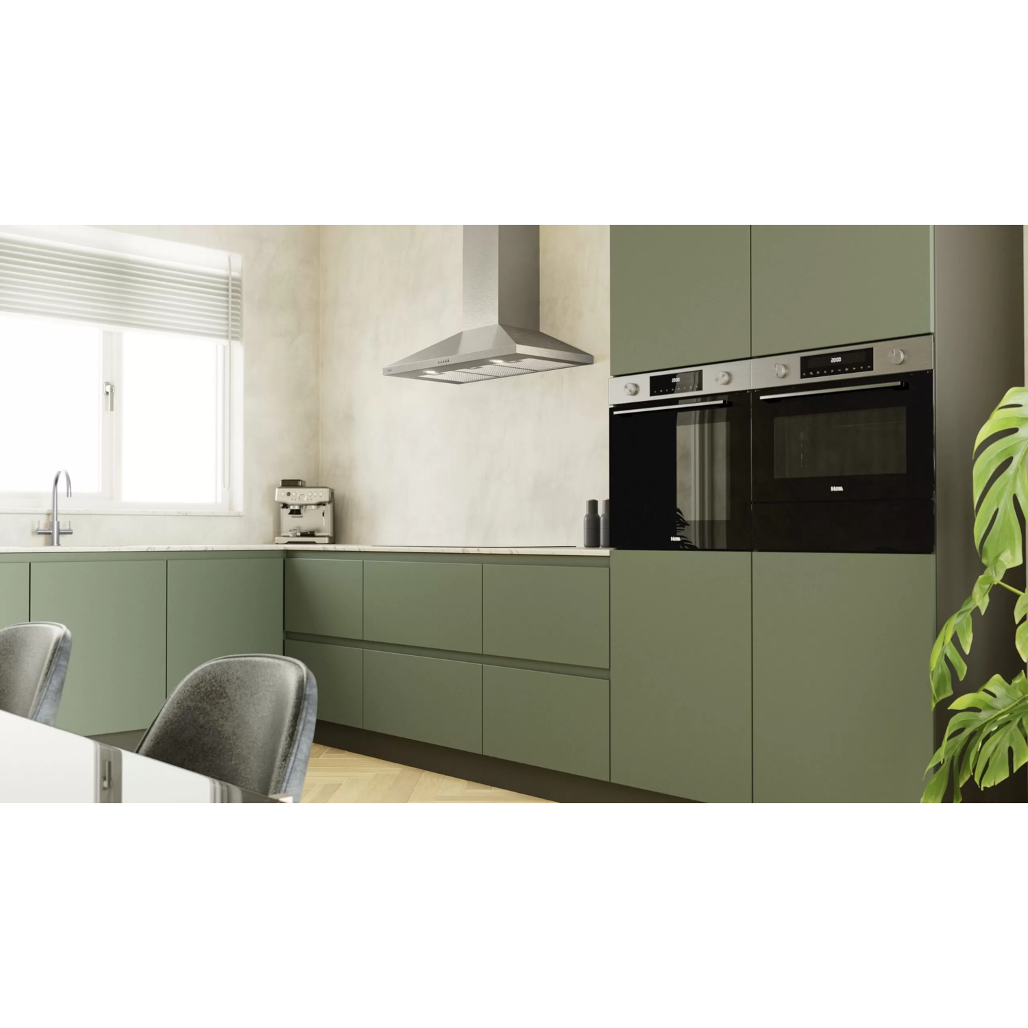 Groene keuken met olijfkasten, roestvrijstalen afzuigkap, inbouwoven en raam.