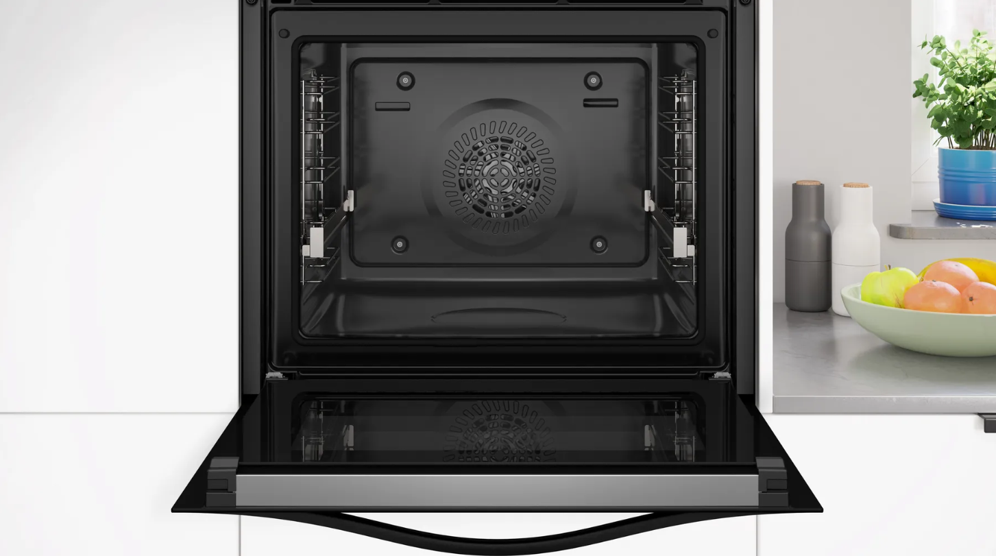 Interior de horno abierto con ventilador superior visible. Cuencos de frutas y recipientes en la encimera, armarios blancos.