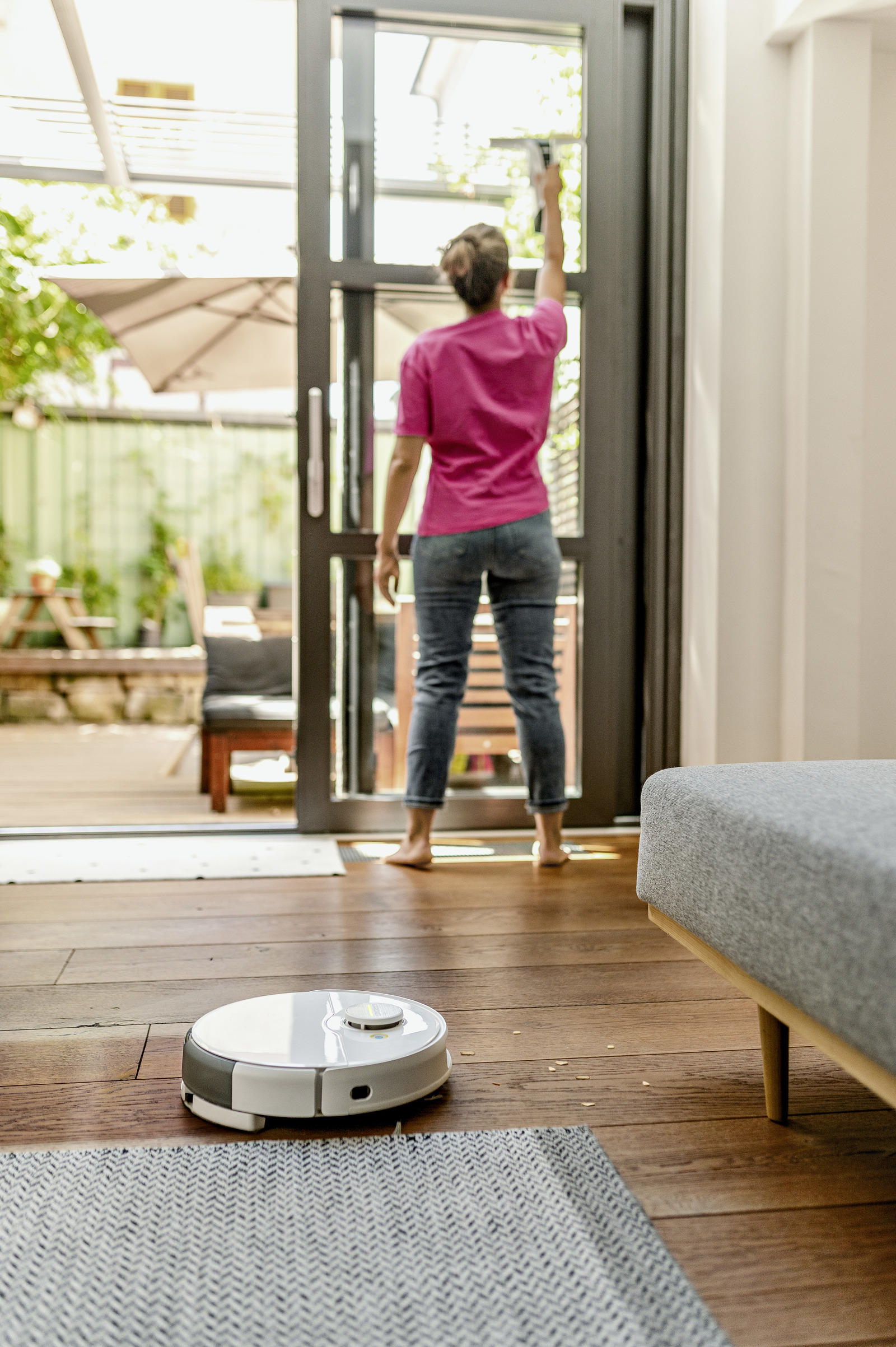 Kobieta czyści szklane drzwi za pomocą robota sprzątającego.