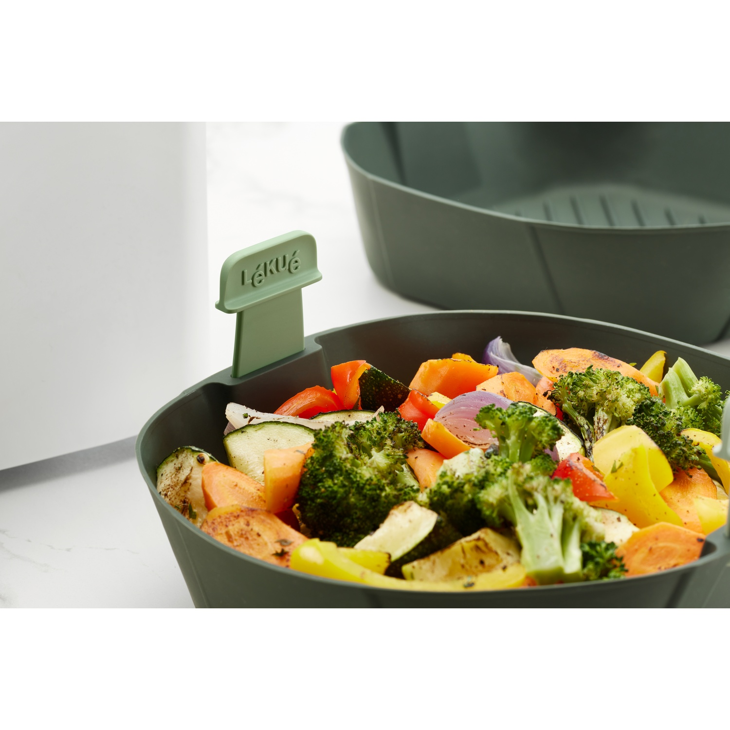 Close-up of a green container filled with cooked vegetables. The LÉKUÉ label is visible.