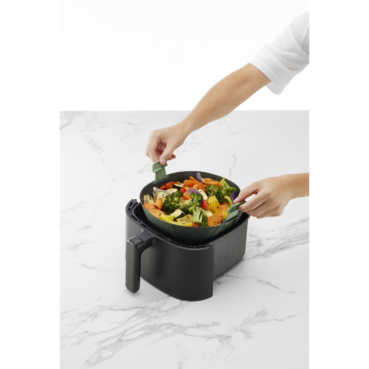 Person placing a bowl of vegetables into an air fryer.