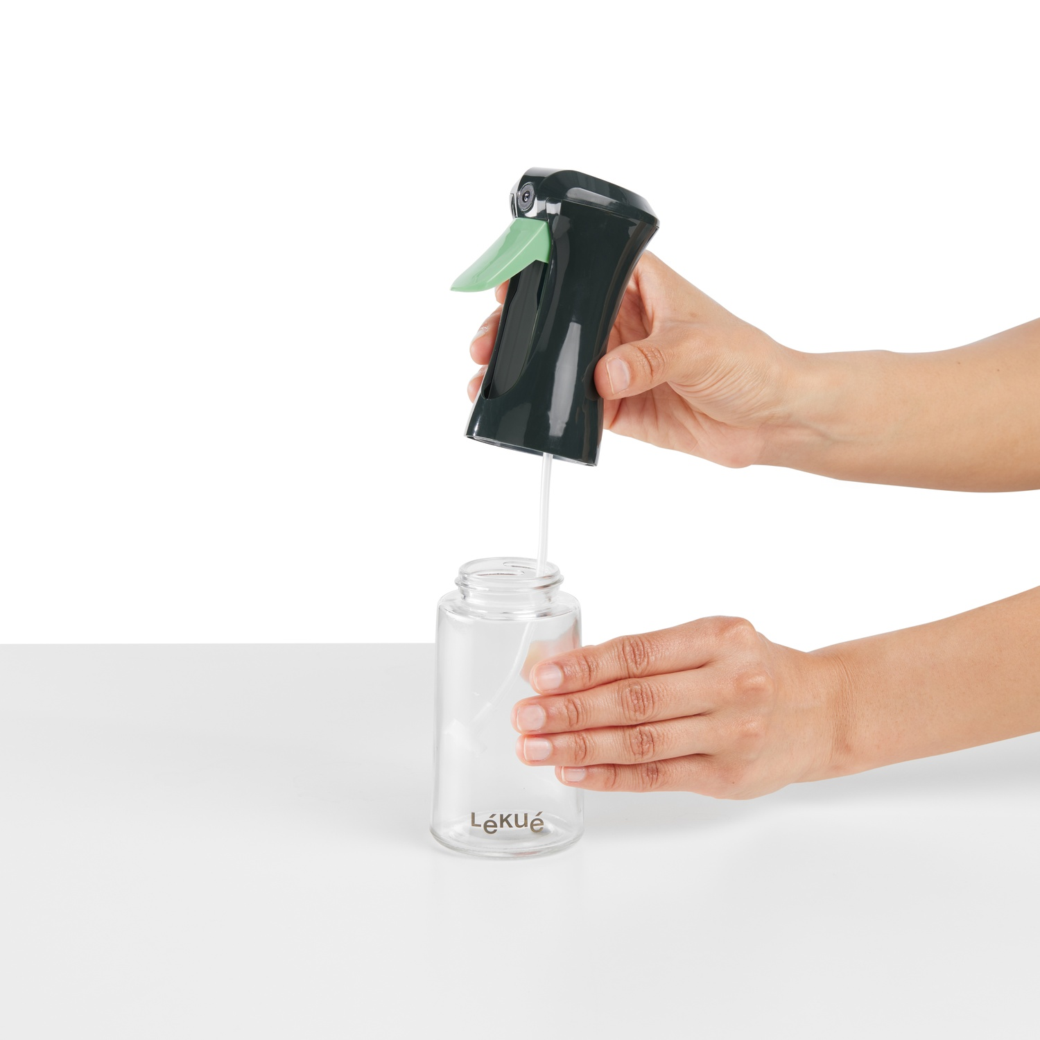 Person assembling a spray bottle with green nozzle. White background.
