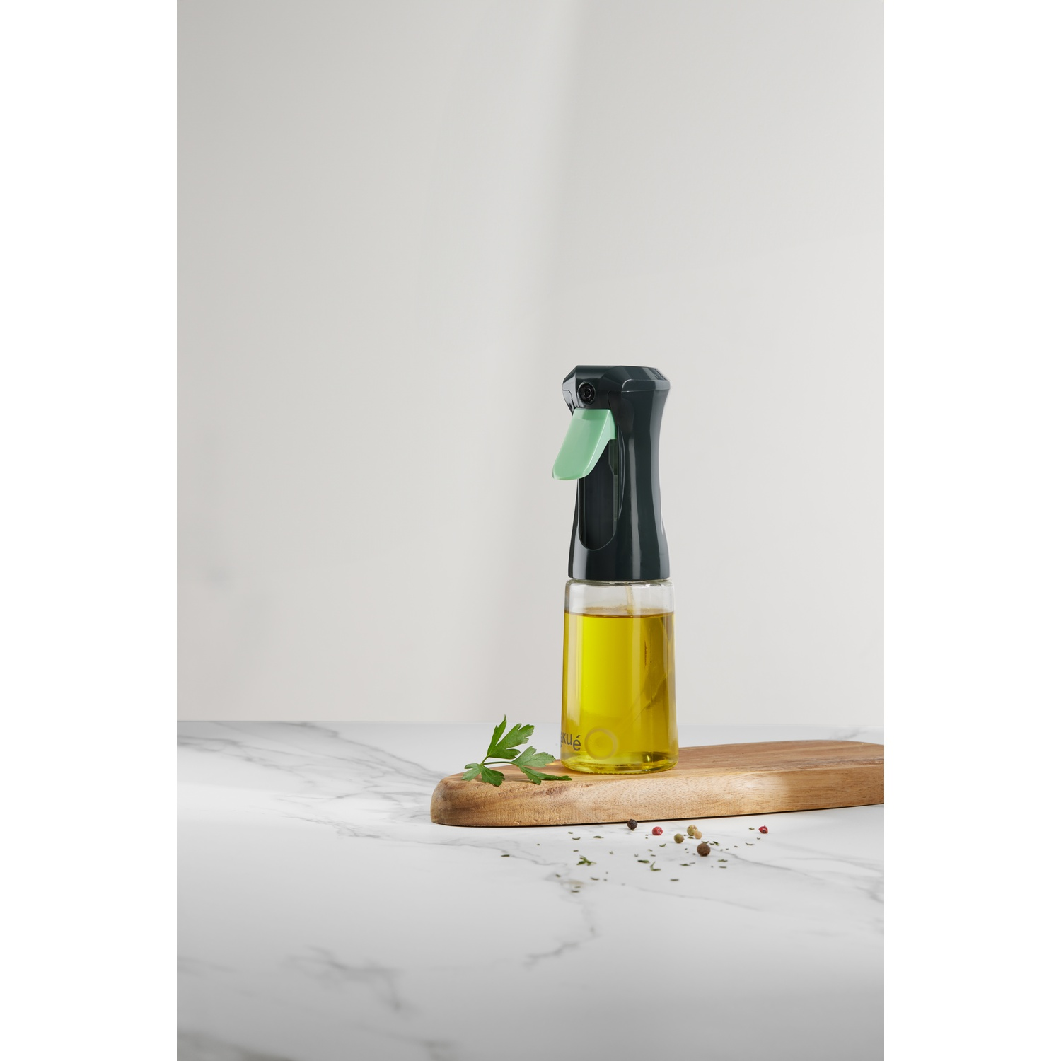 Oil spray bottle with olive oil, on wood board with herbs and spices, white background.